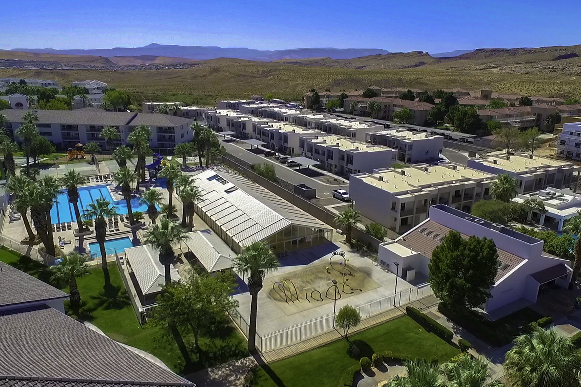 Expansive swimming pool area with multiple rectangular pools and surrounding lounge seating, framed by numerous palm trees