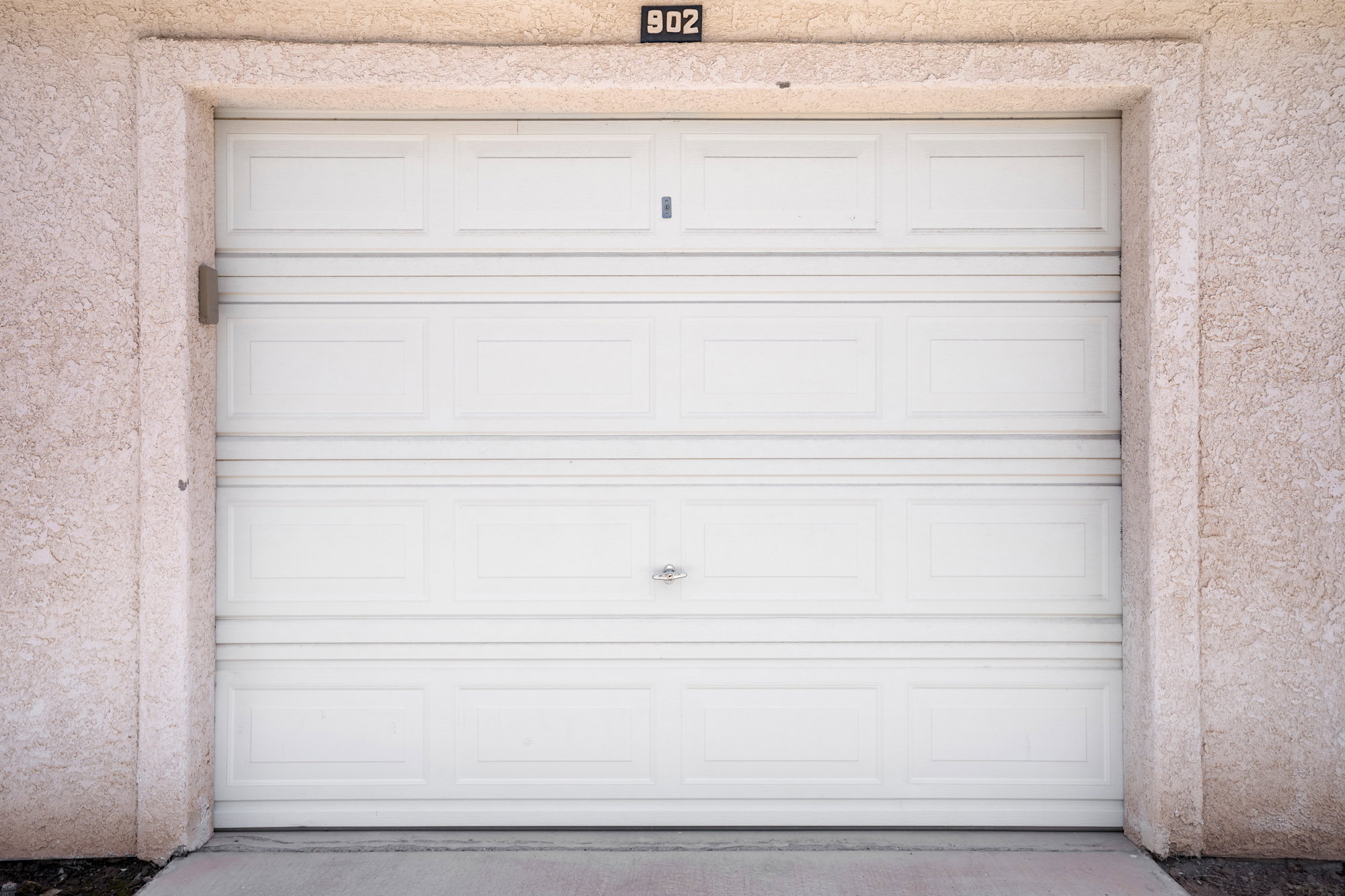 White paneled garage door with a textured stucco surround and integrated address number
