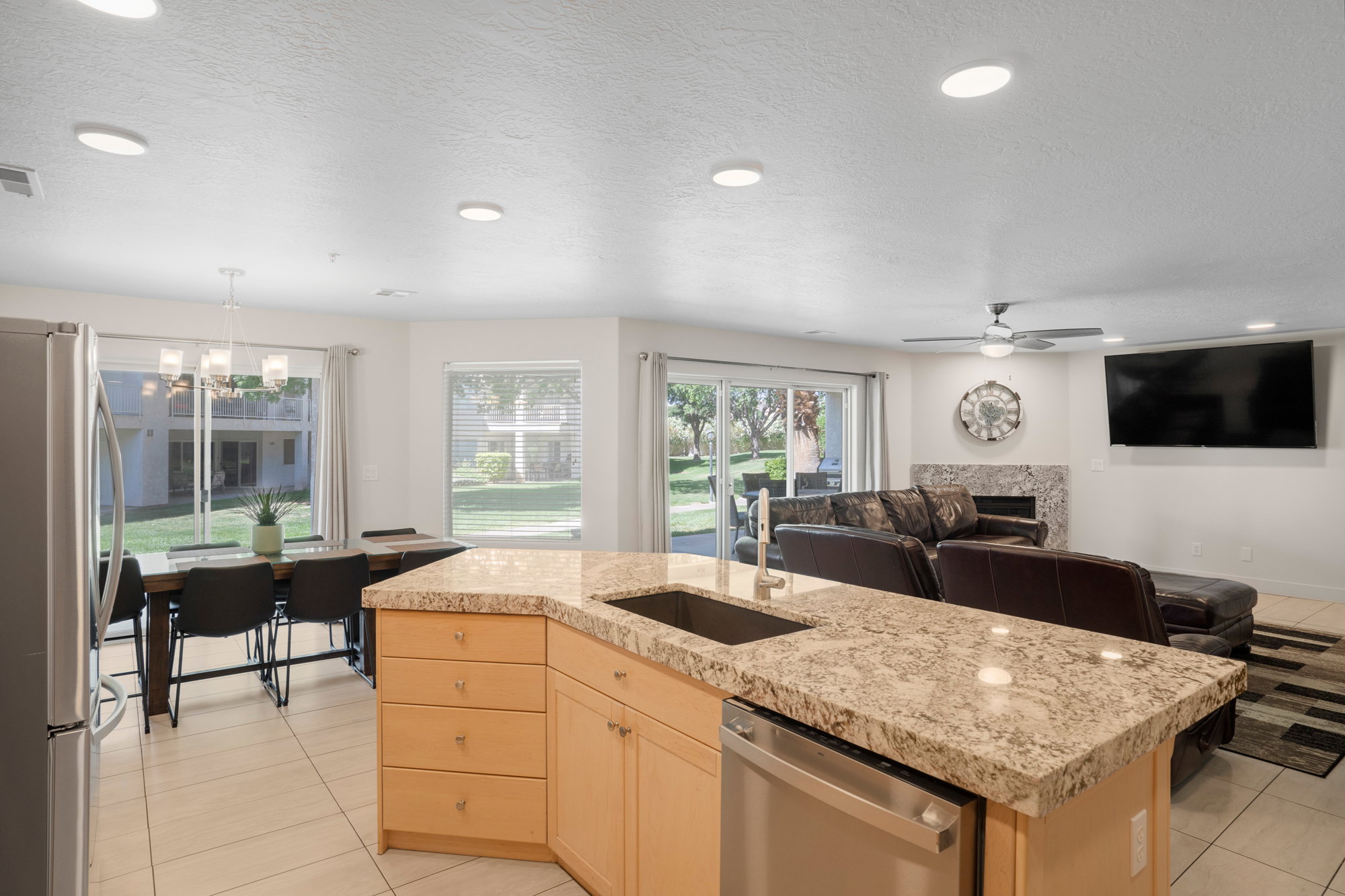 Open-concept living space with a kitchen island featuring a stainless steel sink and dishwasher, light-toned cabinetry, and granite-style countertops