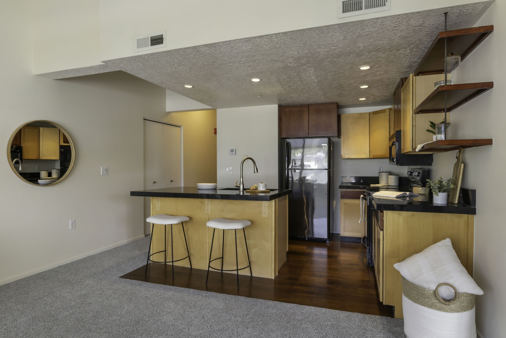 Open-concept kitchen with wood-finish flooring, two-tone cabinetry, black countertops, and a breakfast bar island featuring a stainless steel sink