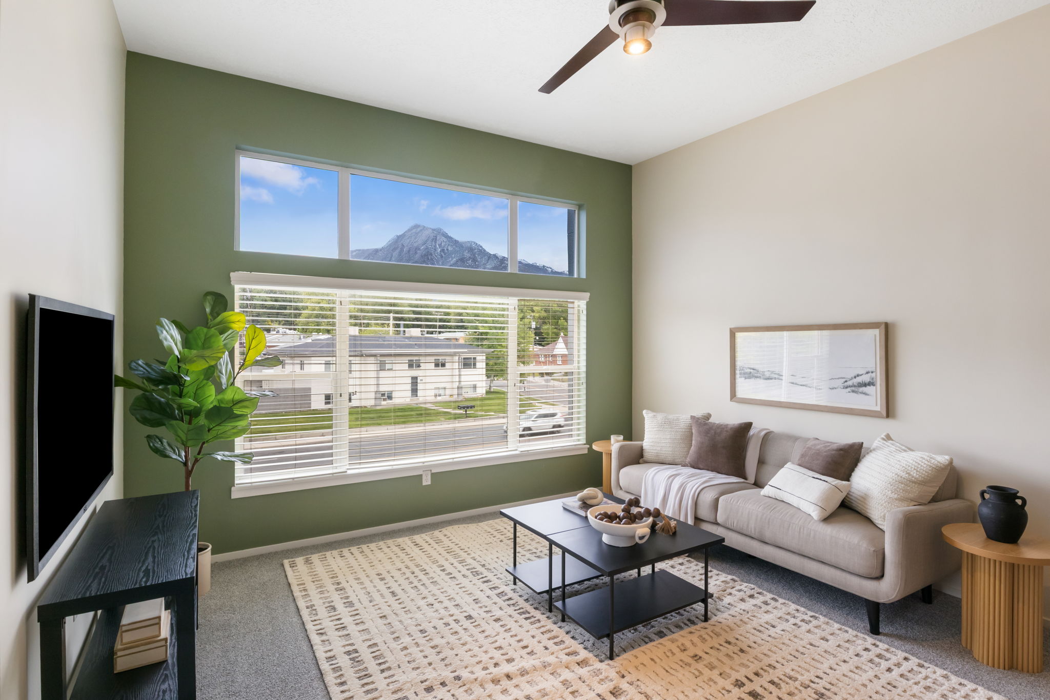 Living area featuring a high ceiling with a ceiling fan, a large picture window with blinds, and an upper transom window