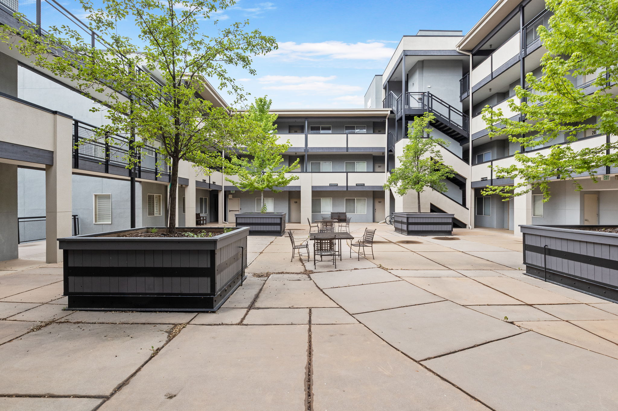 Central courtyard featuring concrete paving, several large planter boxes with established trees, and a dedicated outdoor seating area