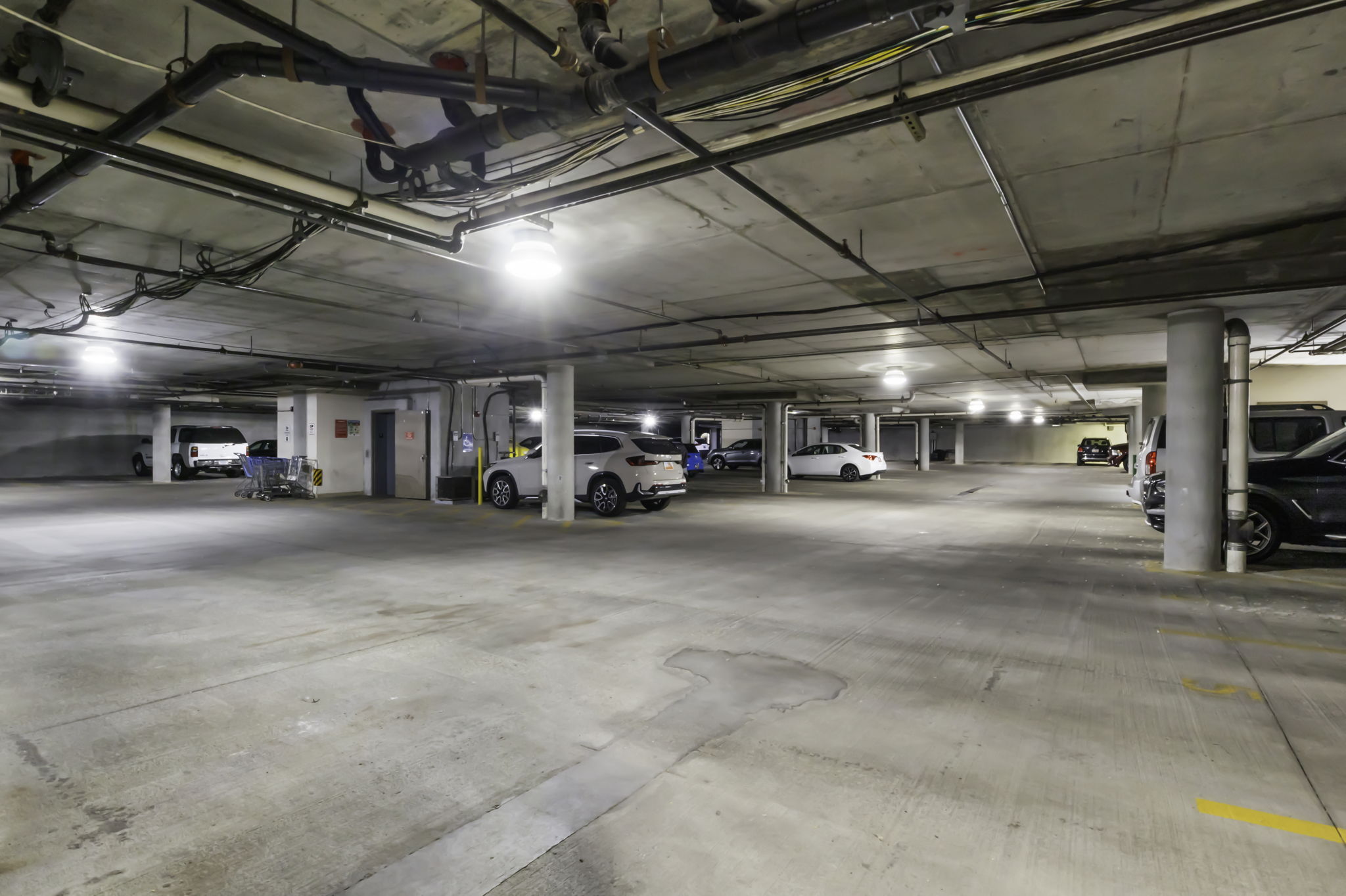 Subterranean concrete parking garage with exposed ceiling pipes and columns