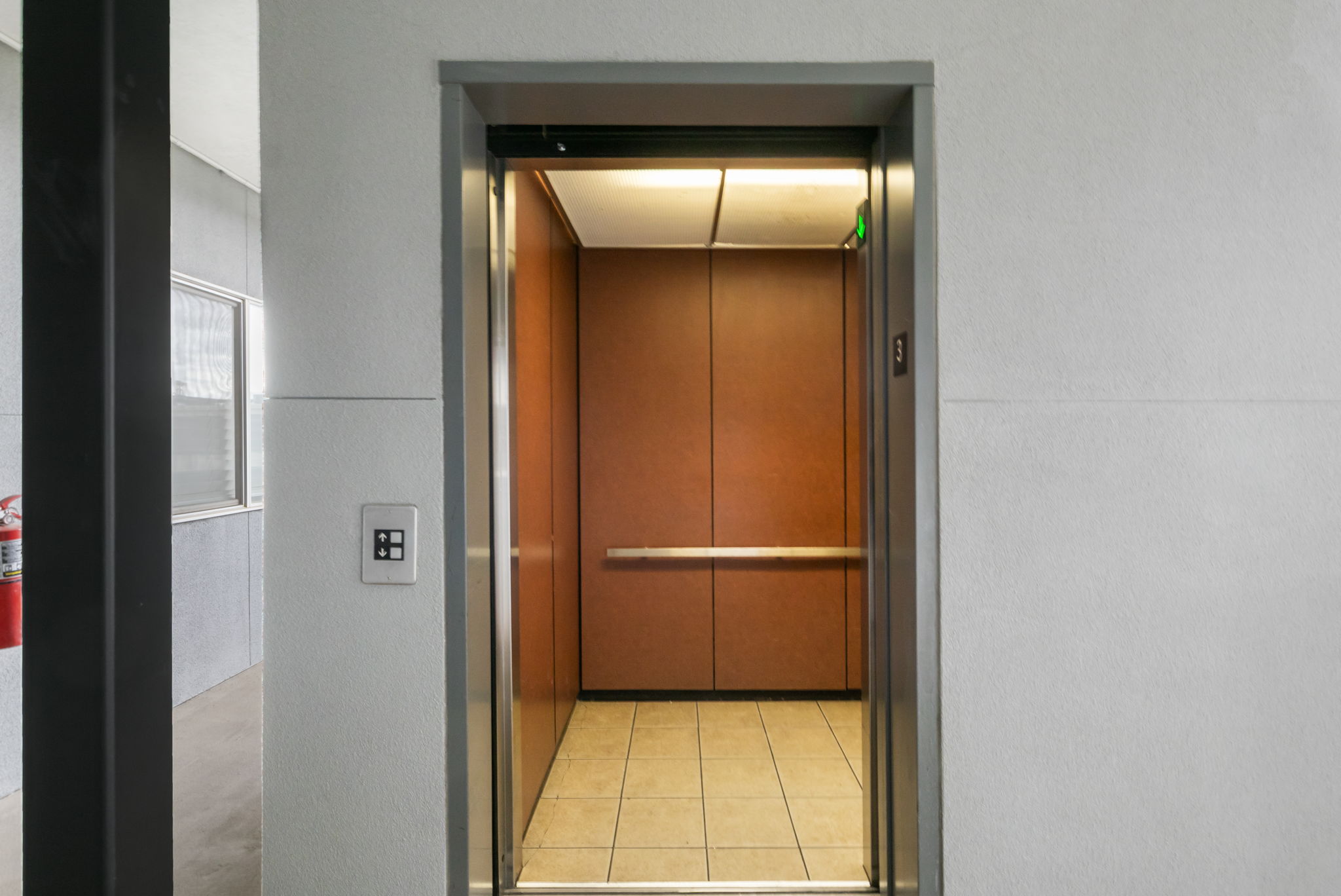 Elevator interior featuring wood-panel walls, illuminated ceiling, and light-toned floor tiling