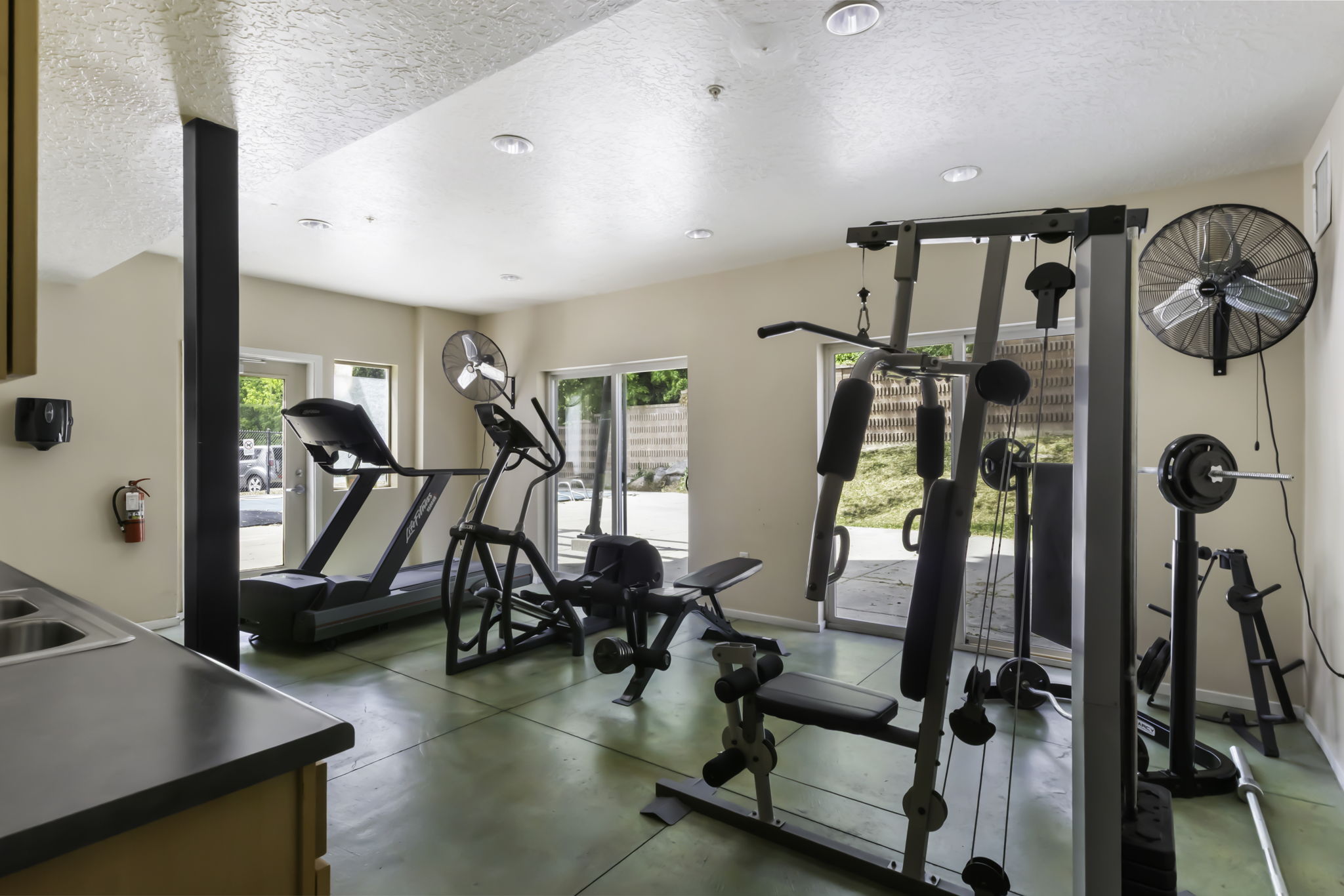 Dedicated fitness area featuring durable green flooring, recessed ceiling lighting, and multiple large glass doors providing abundant natural light