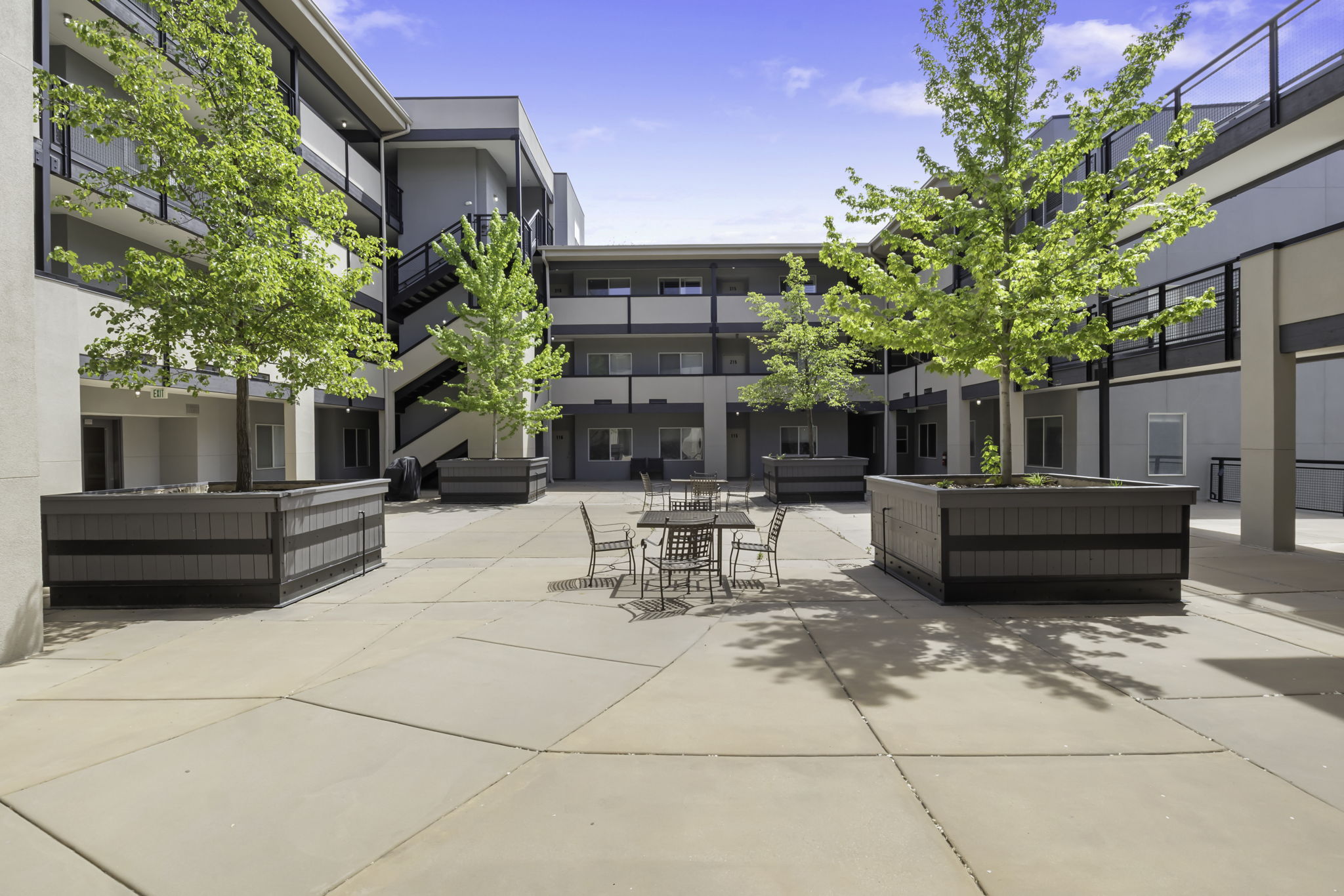 Central courtyard featuring a concrete patio, integrated planters with mature trees, and multi-story buildings with exterior walkways