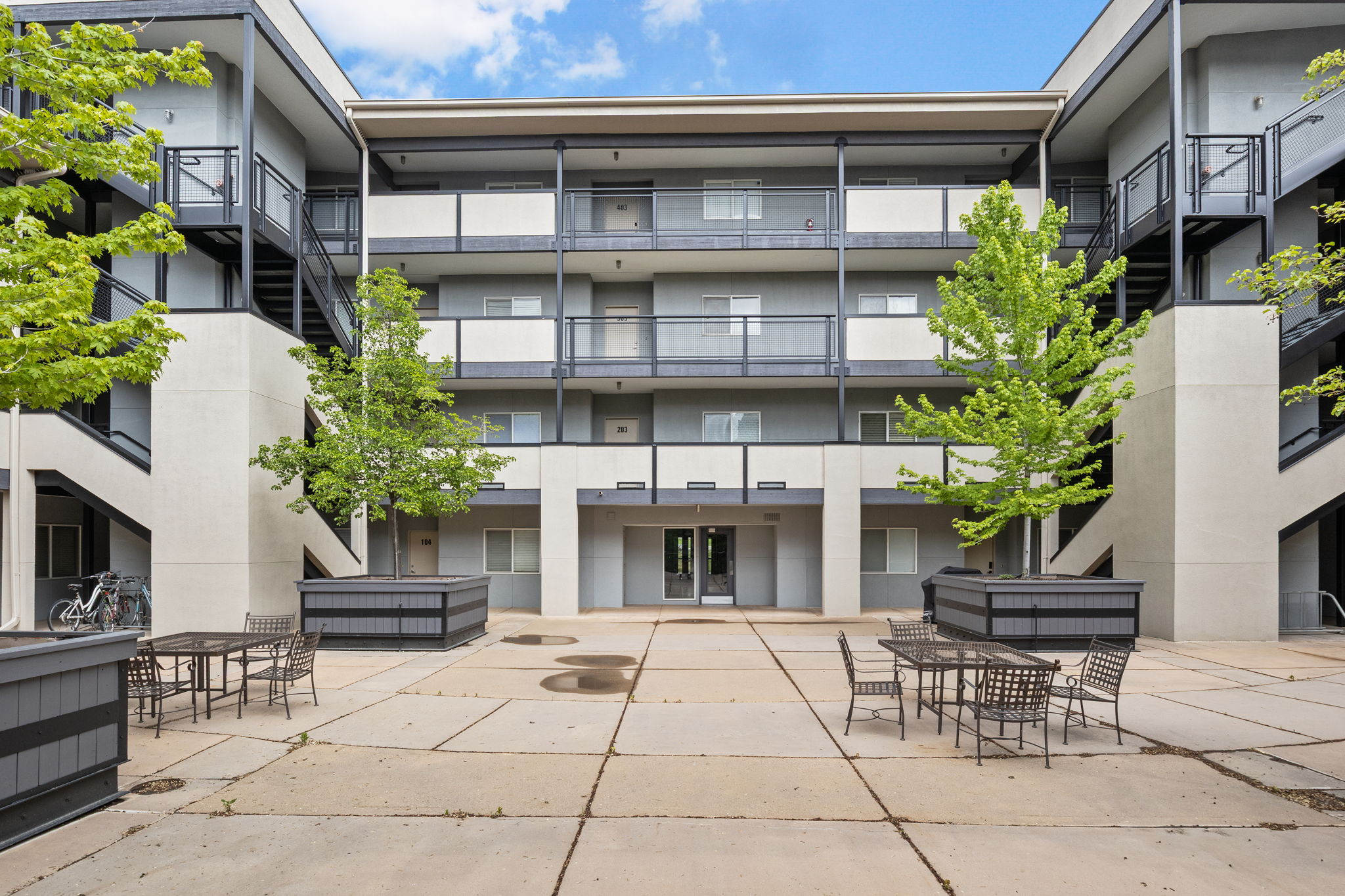 Courtyard entry featuring concrete paving, mature trees in planters, and multi-level building access