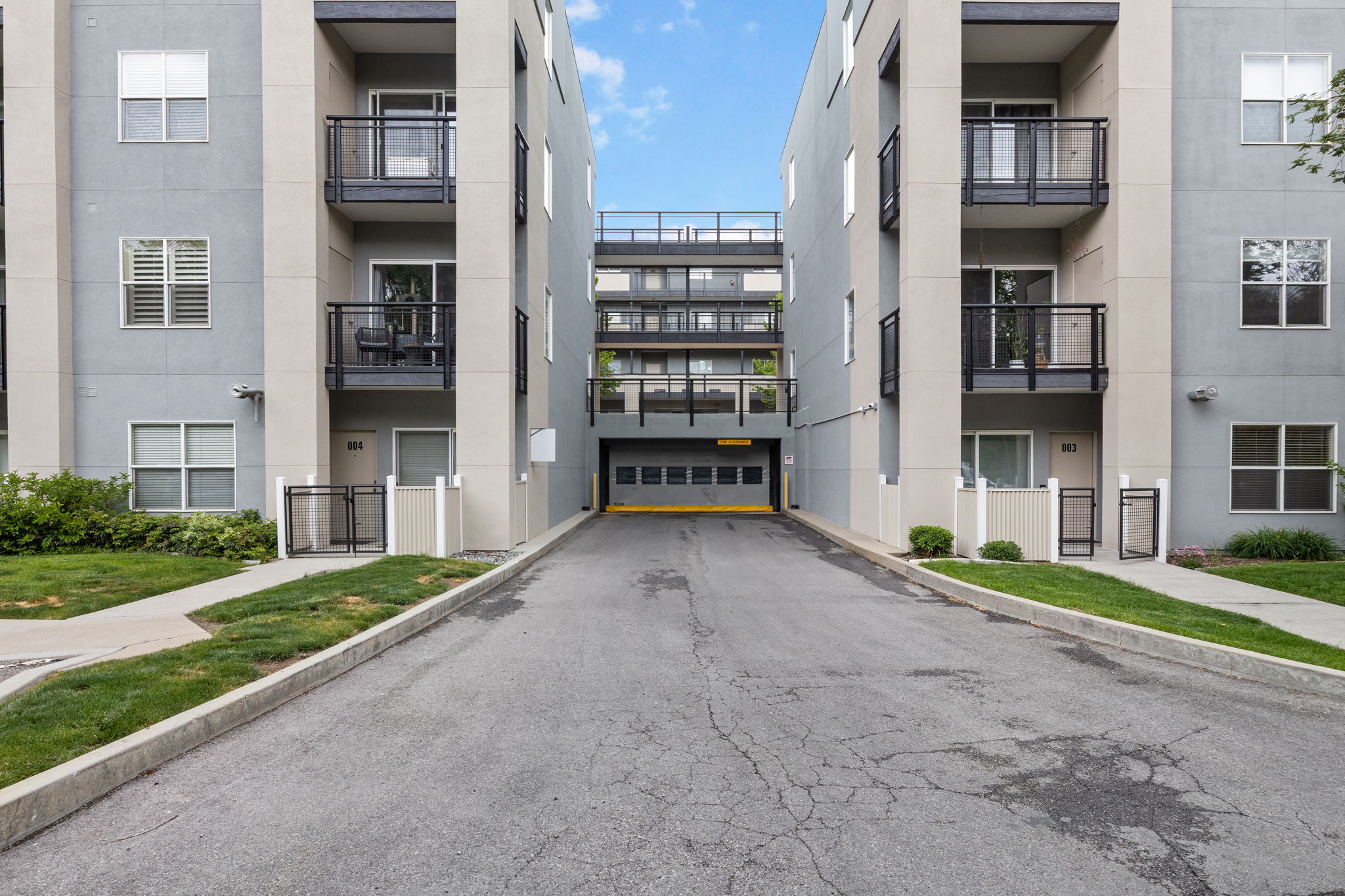 Modern multi-story building exterior featuring balconies with black railings, grey and beige siding, and a subterranean parking garage entrance