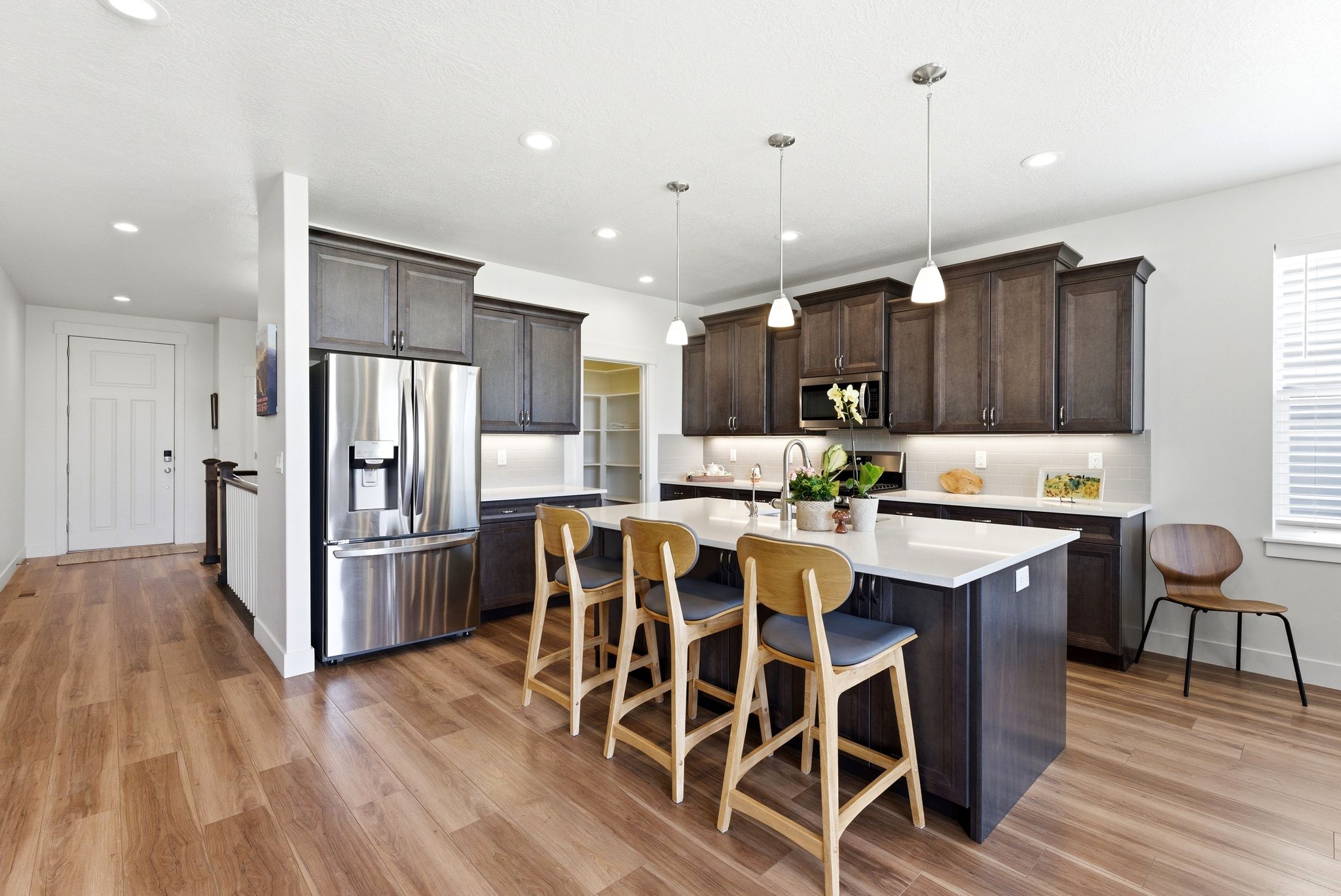 Kitchen featuring a central island with countertop seating, wood-finish flooring, stainless steel French door refrigerator, dark wood cabinetry with crown molding, and recessed lighting