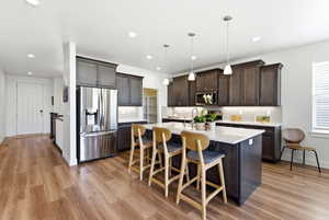 Kitchen featuring a central island with countertop seating, wood-finish flooring, stainless steel French door refrigerator, dark wood cabinetry with crown molding, and recessed lighting