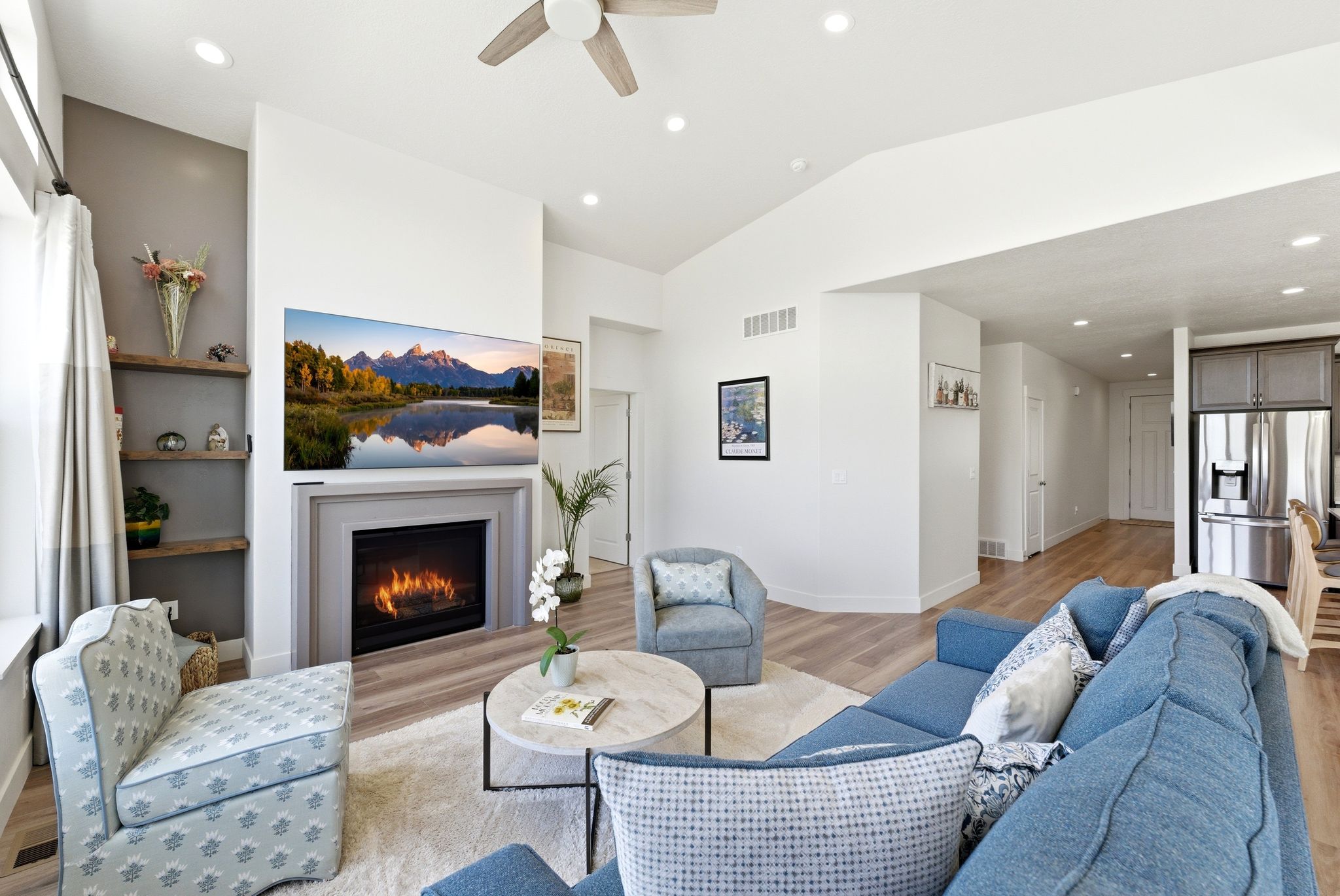 Living area featuring a central fireplace with a grey surround, wood-finish flooring, recessed lighting, and vaulted ceilings