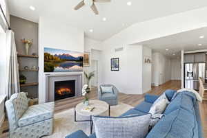 Living area featuring a central fireplace with a grey surround, wood-finish flooring, recessed lighting, and vaulted ceilings