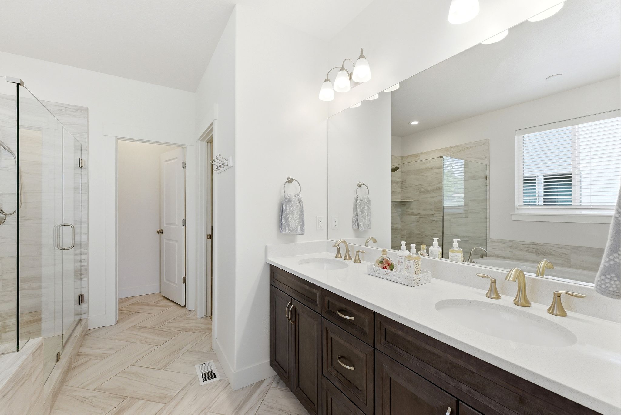 Double vanity with dark wood-finish cabinetry, white countertops, and gold-toned fixtures
