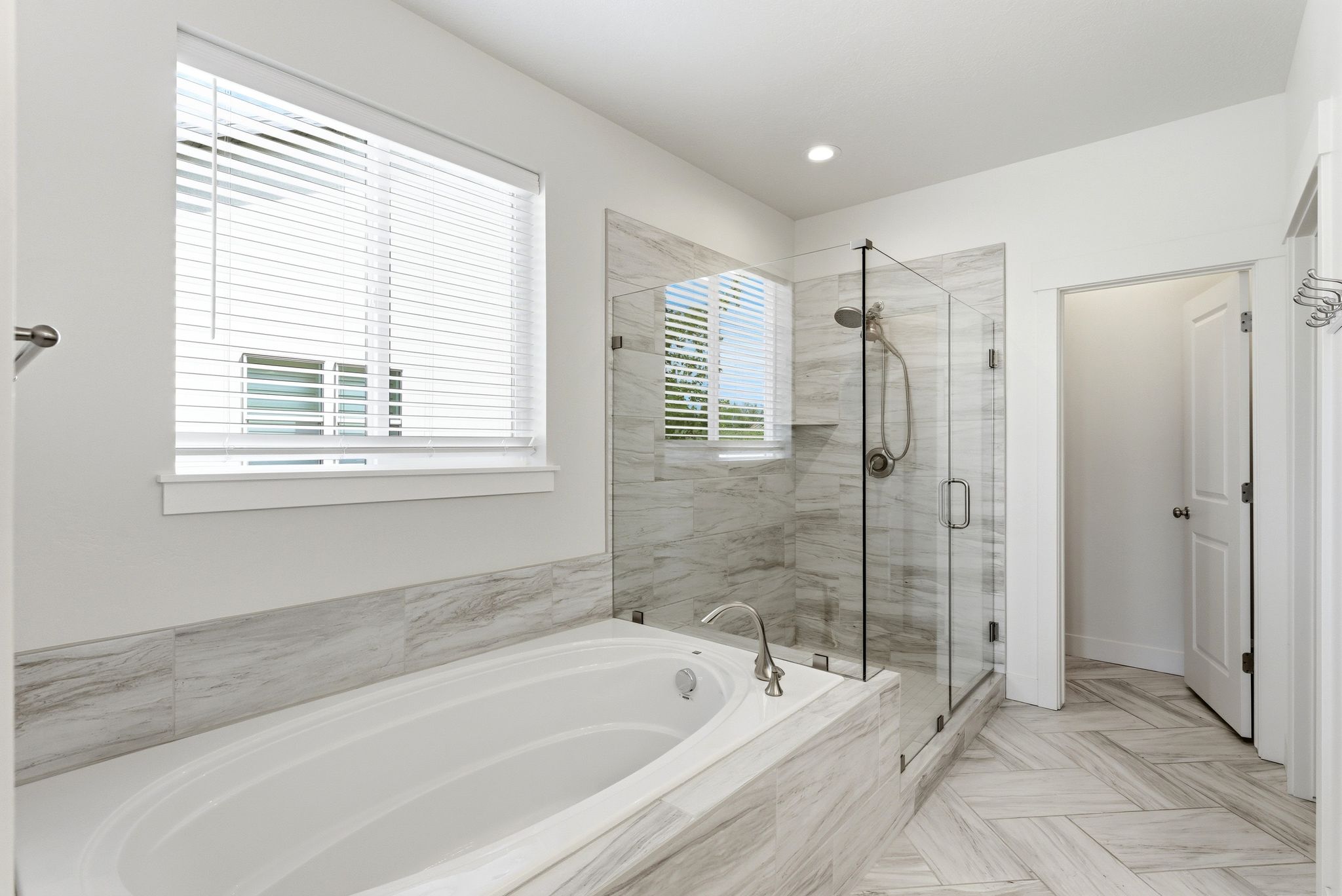 Spacious bathroom featuring a built-in soaking tub, a frameless glass shower enclosure with a built-in niche, floor-to-ceiling tile in the shower, large format tile surrounding the tub, and herringbone pattern tile flooring