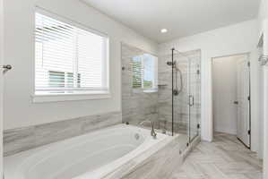 Spacious bathroom featuring a built-in soaking tub, a frameless glass shower enclosure with a built-in niche, floor-to-ceiling tile in the shower, large format tile surrounding the tub, and herringbone pattern tile flooring