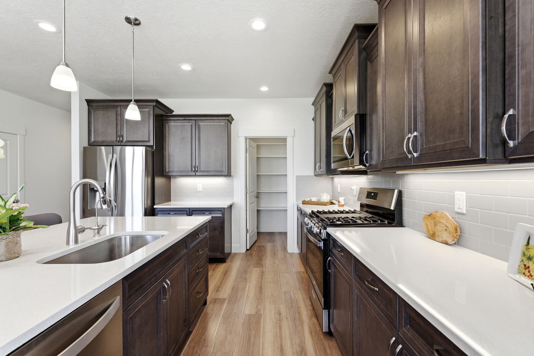 Contemporary kitchen featuring dark wood cabinetry, light countertops, stainless steel appliances, and wood-finish flooring