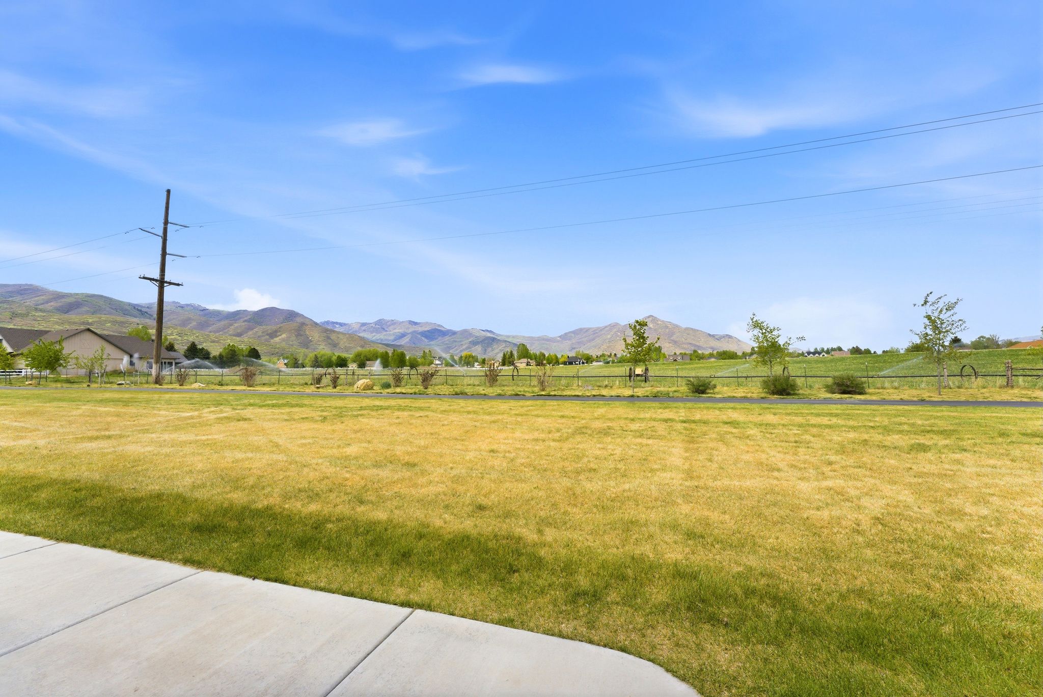 Expansive green space with distant mountain scenery, featuring a paved pathway and partial residential structures