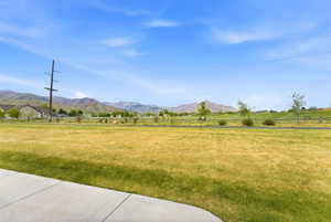 Expansive green space with distant mountain scenery, featuring a paved pathway and partial residential structures