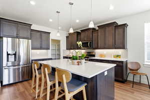 Kitchen featuring a central island with countertop seating, dark wood-finish cabinetry, stainless steel appliances, and wood-finish flooring