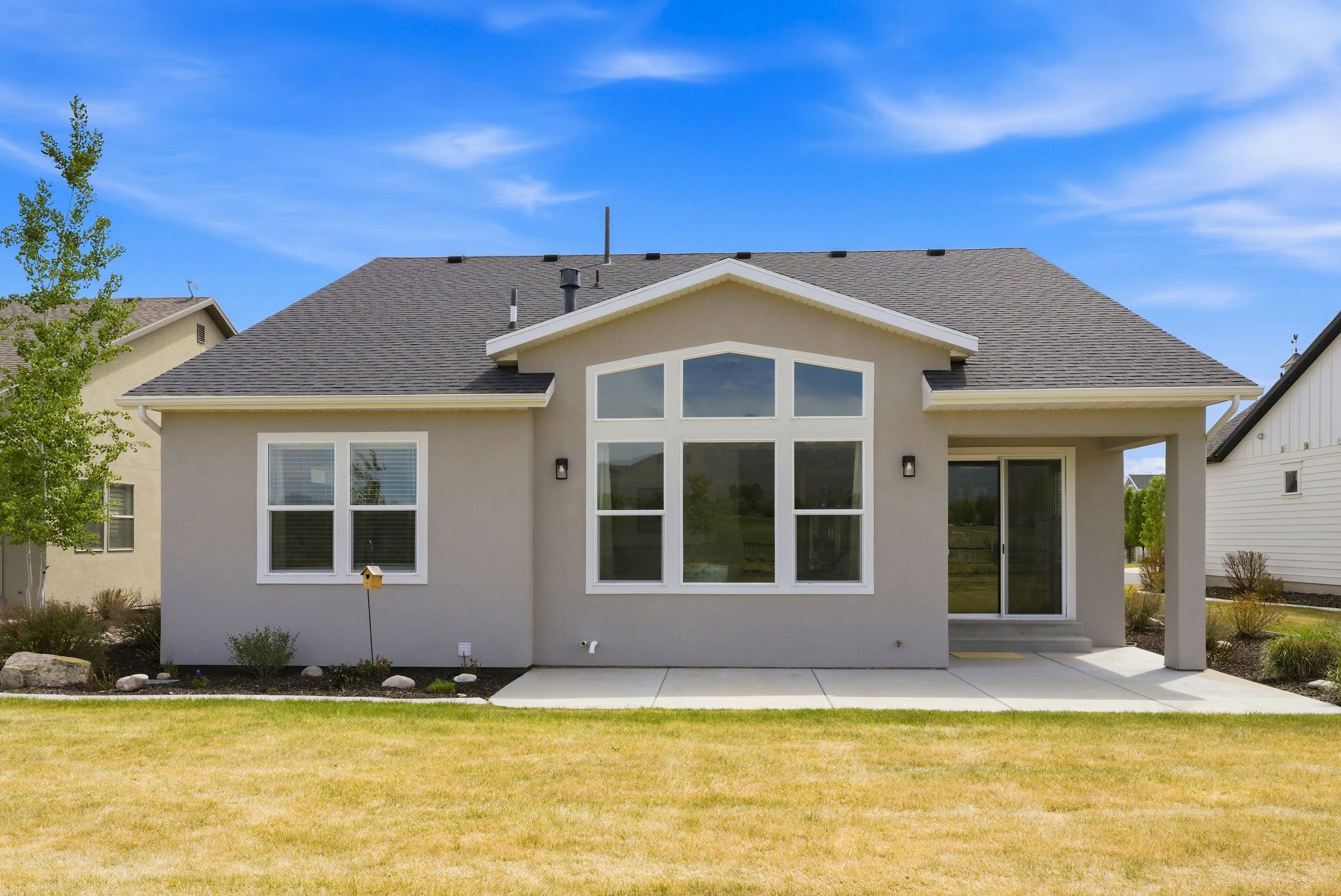 Rear exterior featuring a covered patio, expansive multi-pane windows, and sliding glass doors