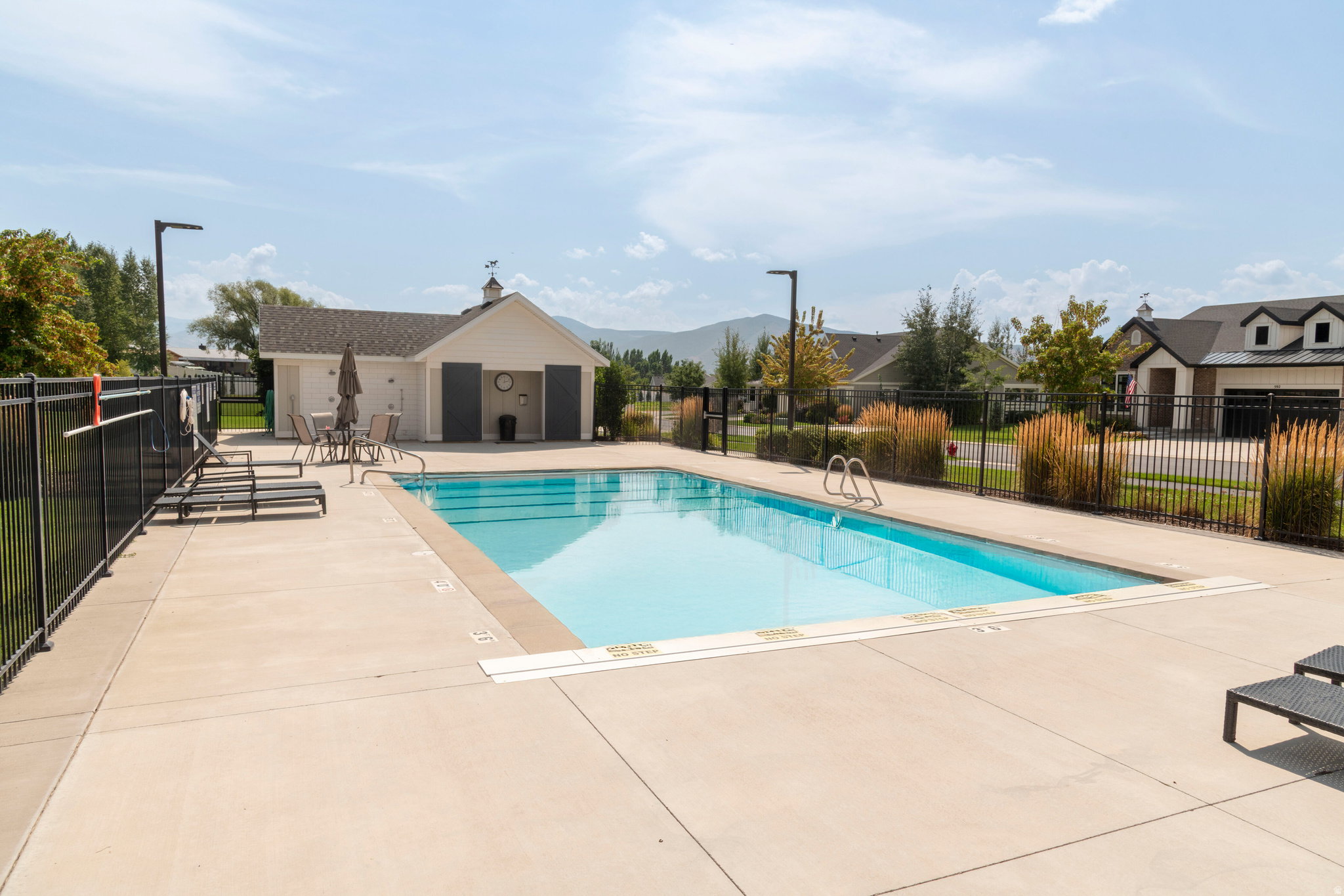 Outdoor swimming pool with integrated steps, surrounded by a concrete deck and black metal fencing