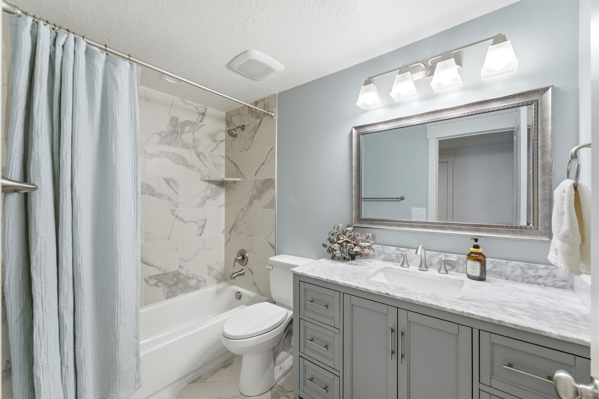 Bathroom featuring a built-in tub with tile surround, a single vanity with a stone countertop, an undermount sink, and a framed mirror