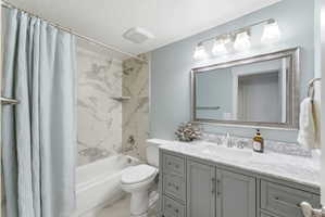 Bathroom featuring a built-in tub with tile surround, a single vanity with a stone countertop, an undermount sink, and a framed mirror