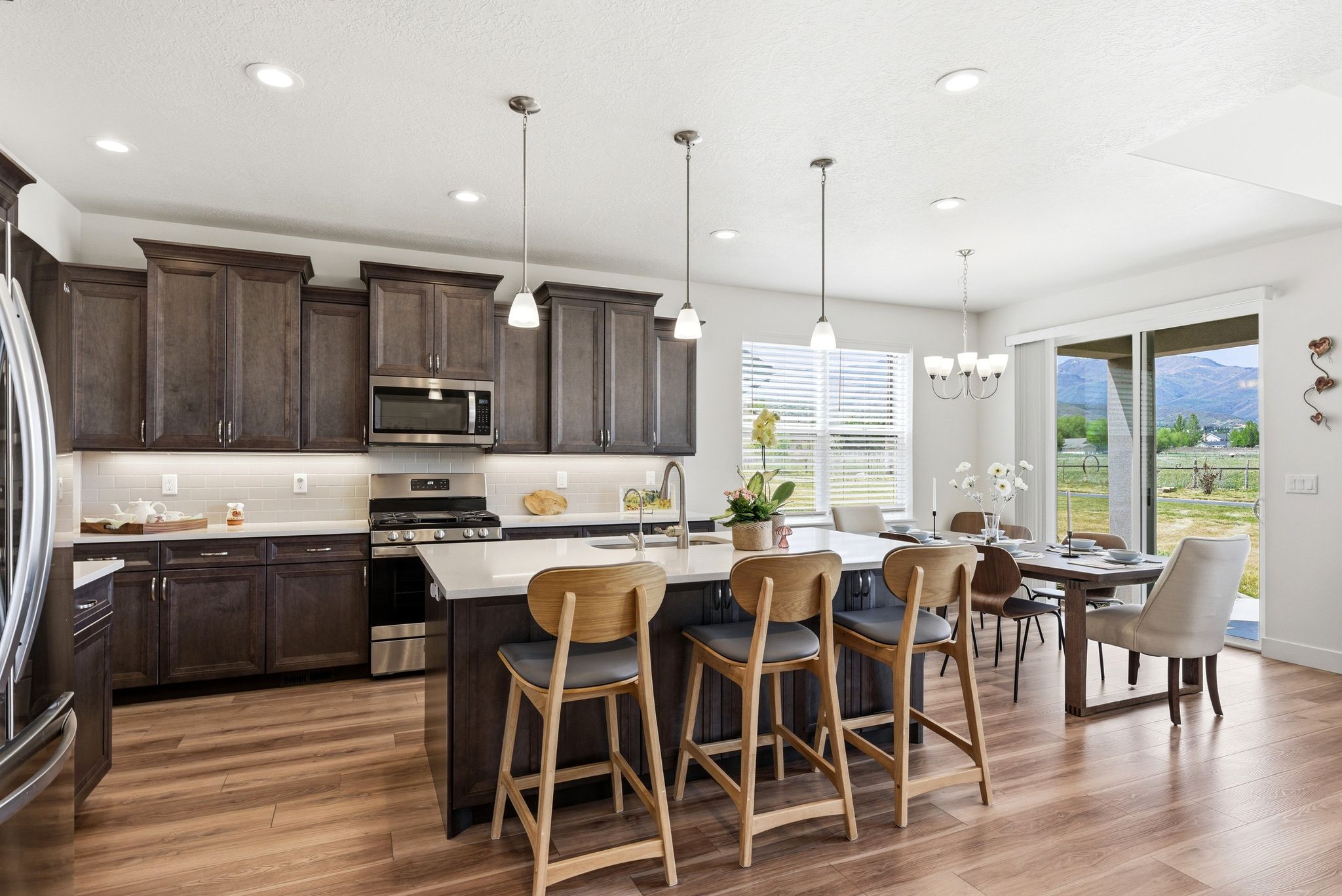 Open-concept kitchen with wood-finish flooring, dark wood cabinetry, white countertops, stainless steel appliances, and a central island with pendant lighting