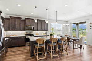 Open-concept kitchen with wood-finish flooring, dark wood cabinetry, white countertops, stainless steel appliances, and a central island with pendant lighting