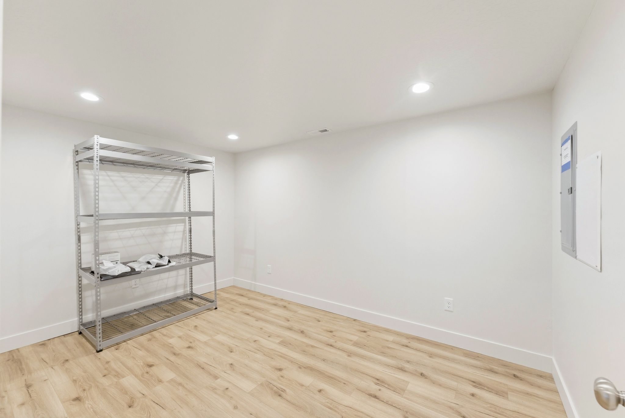 Spacious room featuring wood-finish flooring, white baseboards, recessed lighting, and a neutral color palette