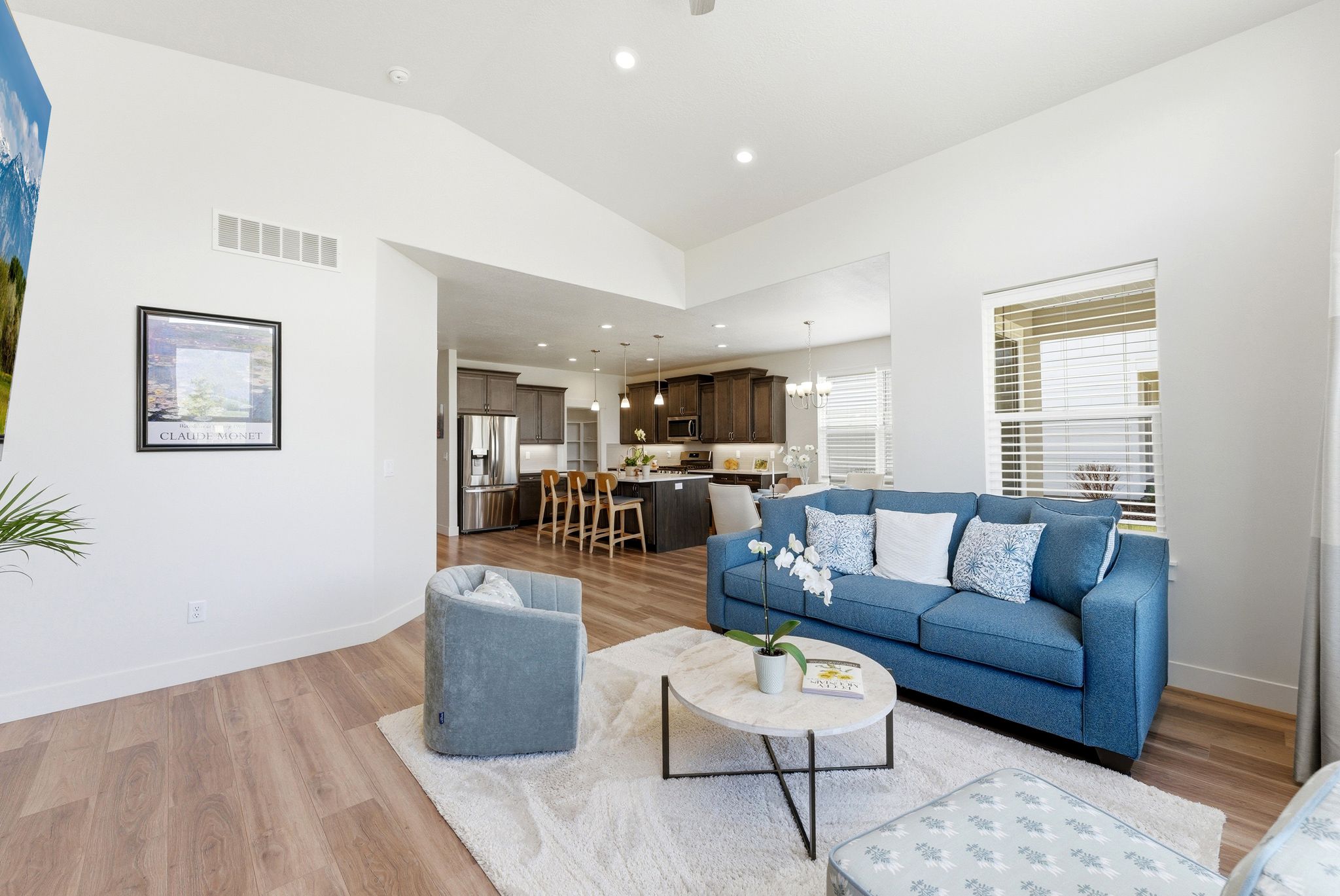 Open-concept living area featuring vaulted ceilings, wood-finish flooring, a kitchen with dark cabinetry, and stainless steel appliances