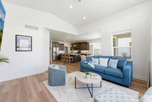Open-concept living area featuring vaulted ceilings, wood-finish flooring, a kitchen with dark cabinetry, and stainless steel appliances
