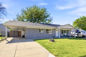 Gray brick exterior with a dark shingle roof, covered carport, covered front porch, and concrete driveway