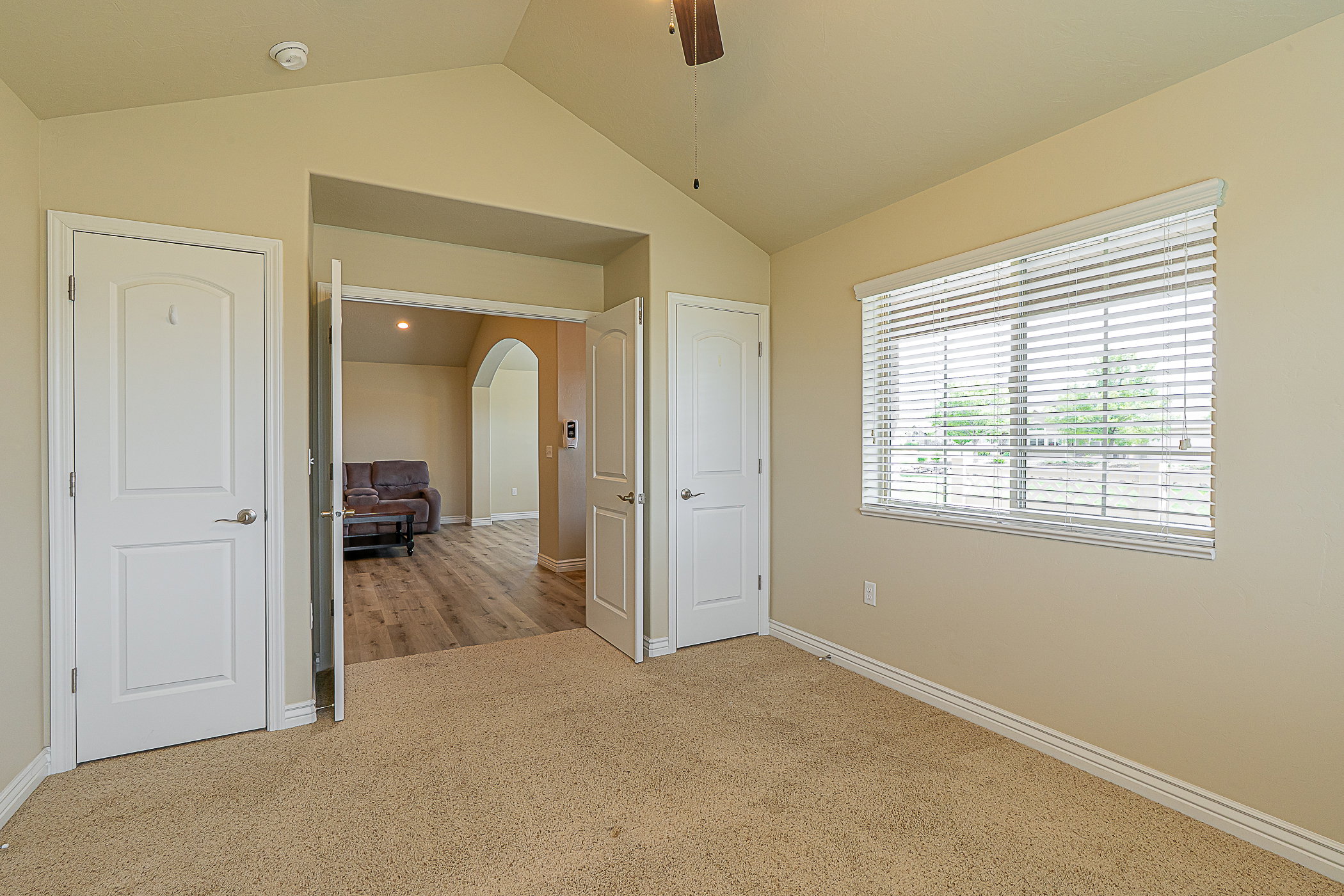 Carpeted room with a vaulted ceiling, a large window featuring horizontal blinds, and a ceiling fan