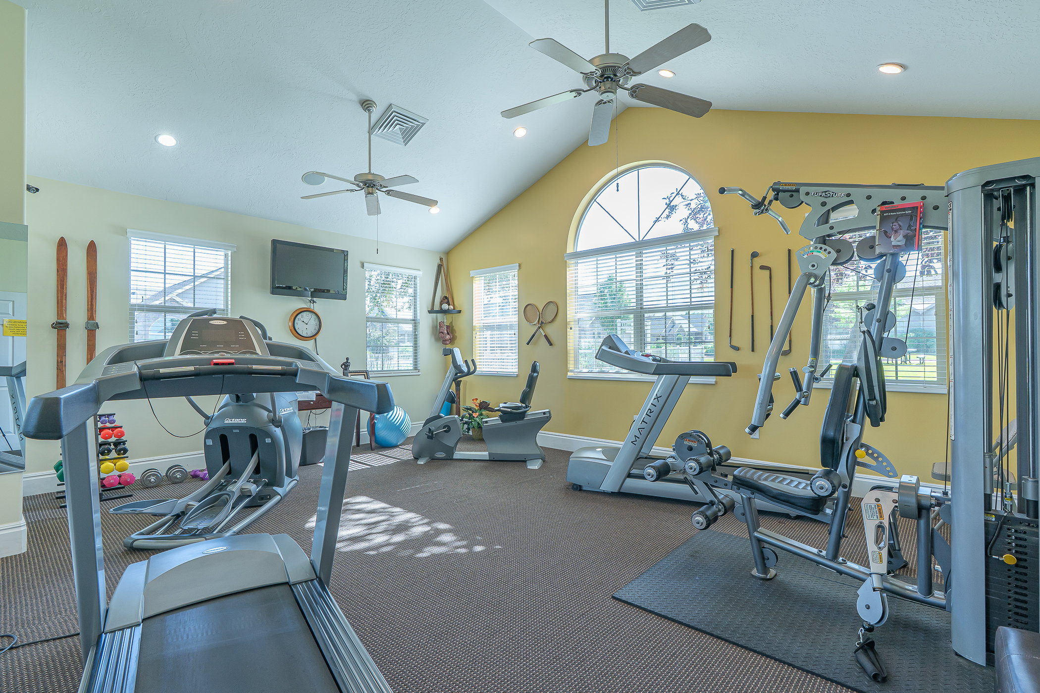 Spacious fitness area featuring vaulted ceilings, recessed lighting, and multiple windows with blinds