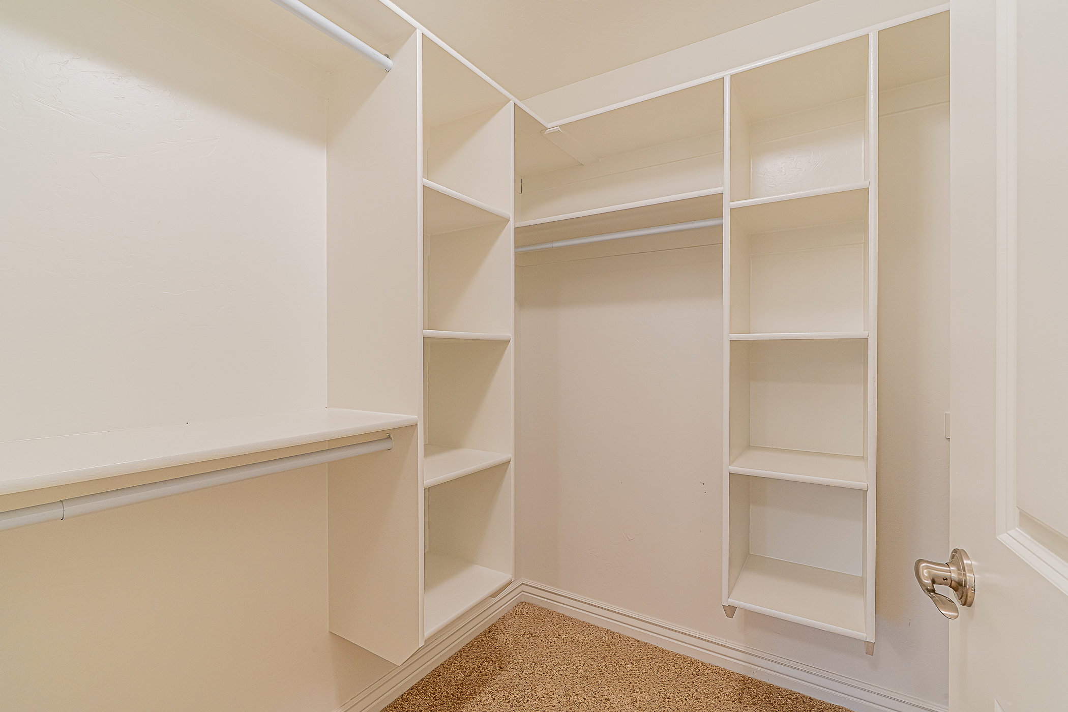 Walk-in closet featuring built-in shelving, multiple hanging rods, and neutral-toned carpeting