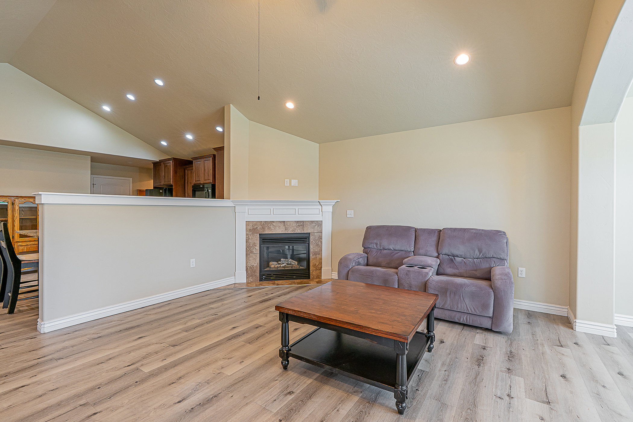 Living area featuring wood-finish flooring, a corner gas fireplace with a tile surround and white mantel, recessed lighting, and vaulted ceilings