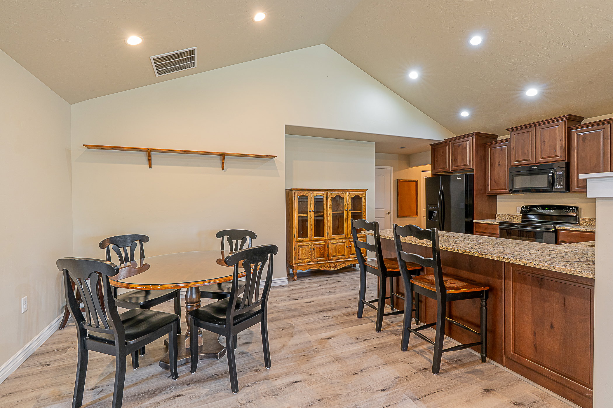 Vaulted ceilings enhance this open concept space featuring wood-finish flooring, recessed lighting, and a breakfast bar with stone countertops