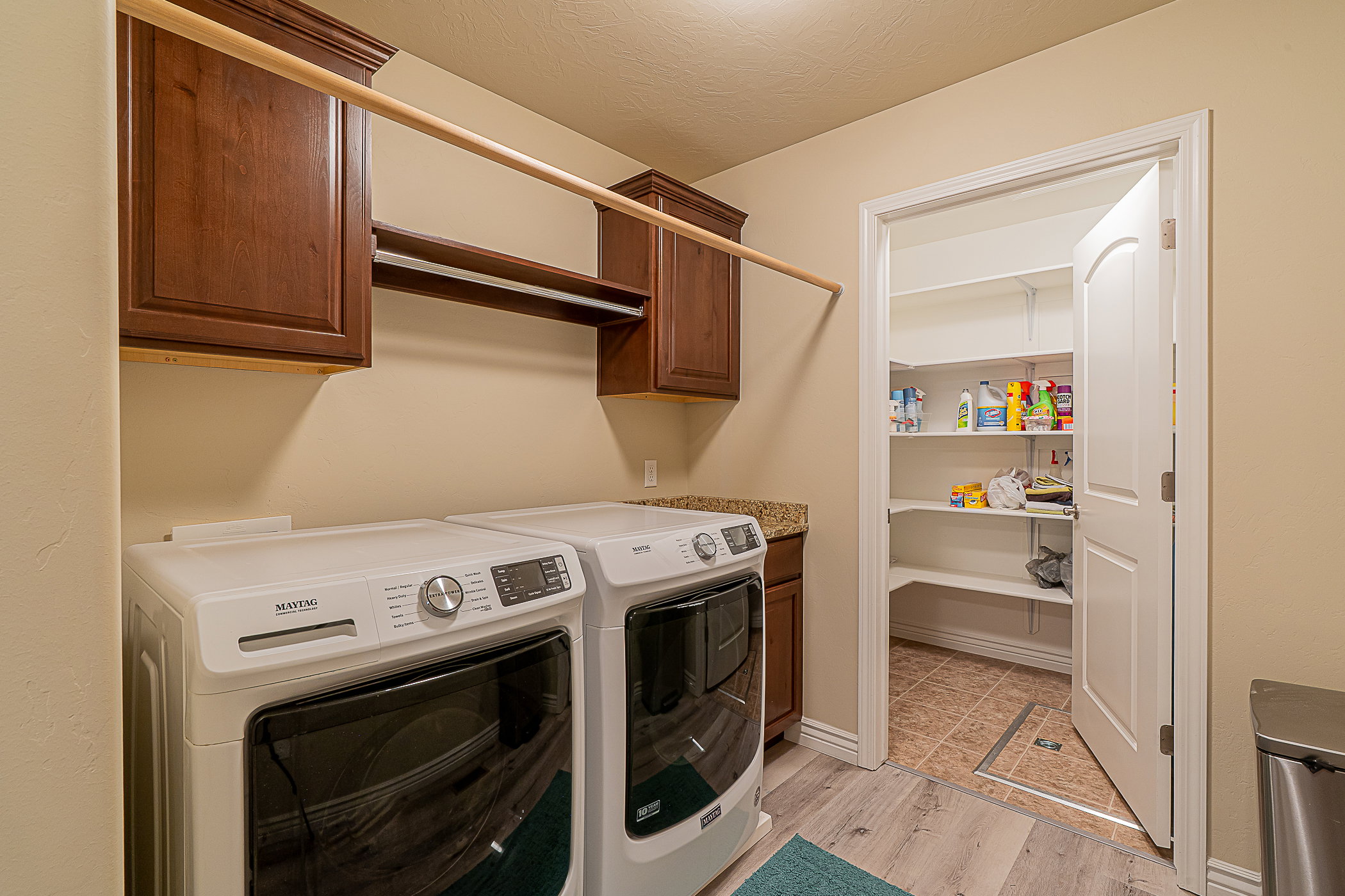 Dedicated utility space featuring wood-finish flooring, dark wood cabinetry, a granite-style countertop, and a built-in hanging rod
