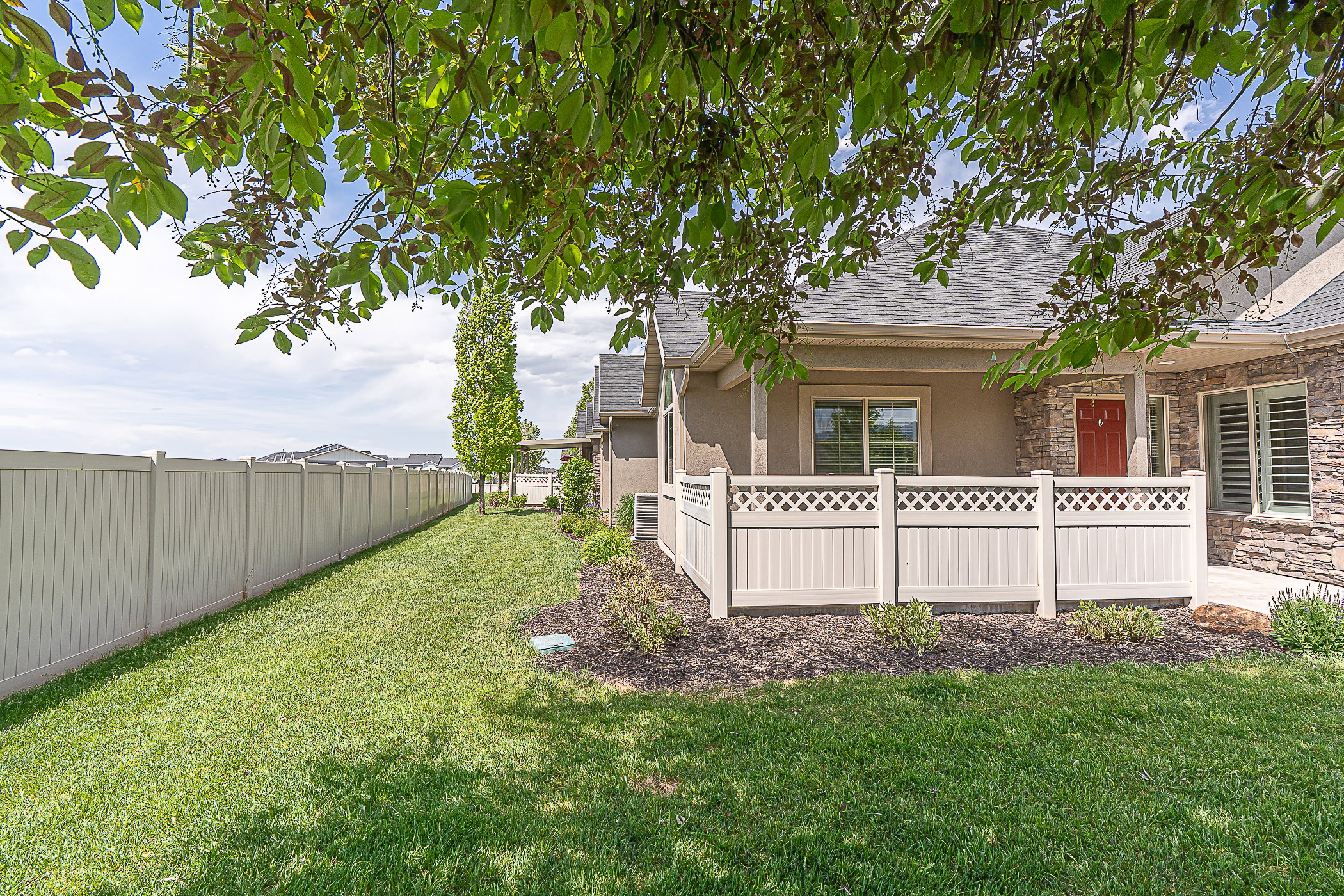 Fenced yard featuring a manicured lawn, a side patio area with lattice detailing, and mature landscaping
