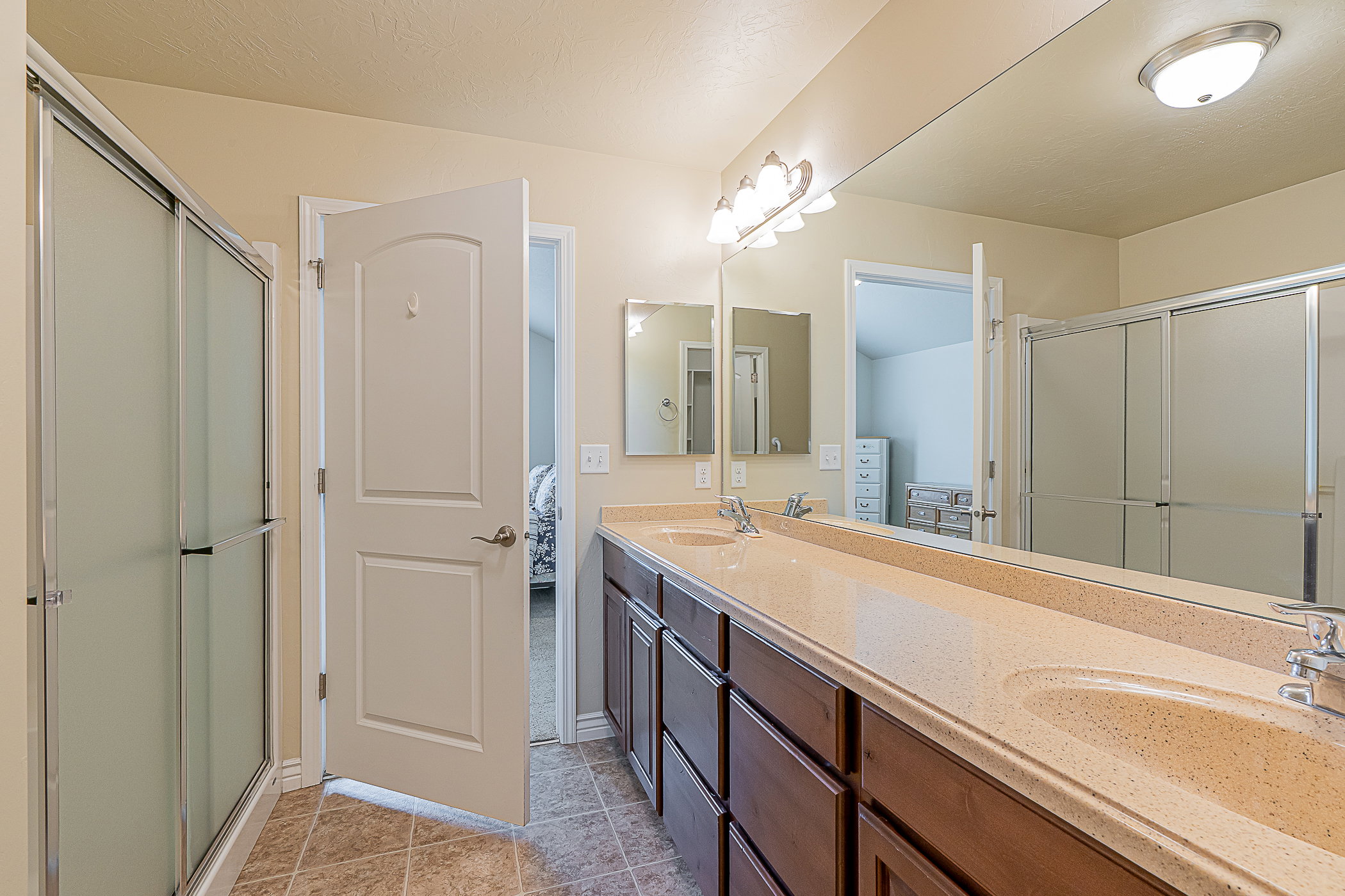 Bathroom featuring a dual vanity with a light-toned countertop, rich wood-finish cabinetry, and an integrated full-width mirror