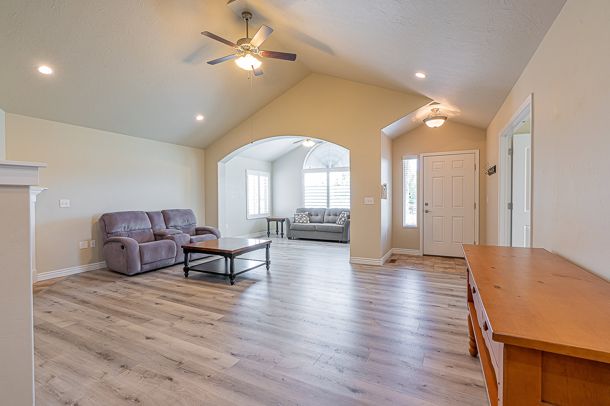 Vaulted ceilings with recessed lighting and a ceiling fan, wood-finish flooring, arched doorway, and white paneled entry door with sidelight