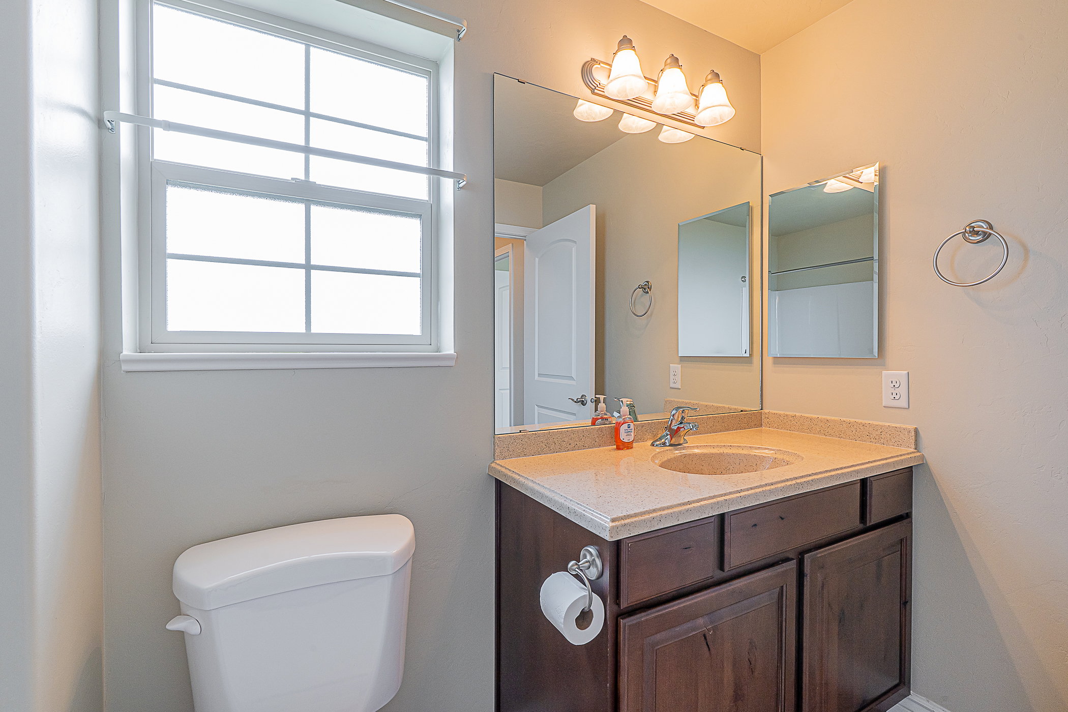 Bathroom featuring a single-sink vanity with a light-toned countertop, dark wood-finish cabinetry, a large wall mirror, and a multi-bulb vanity light fixture