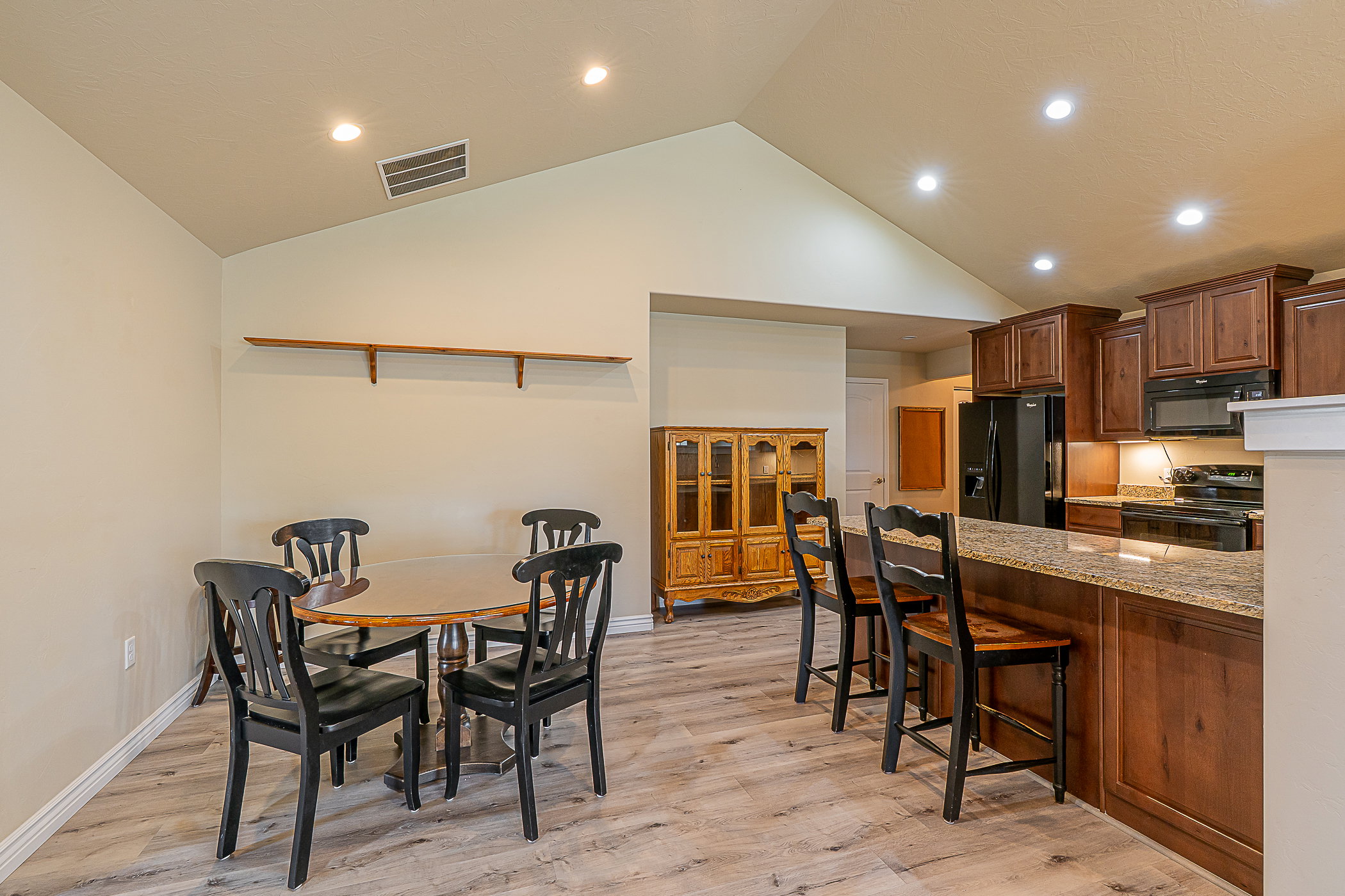Vaulted ceiling dining area featuring recessed lighting, wood-finish flooring, and two wall-mounted shelves