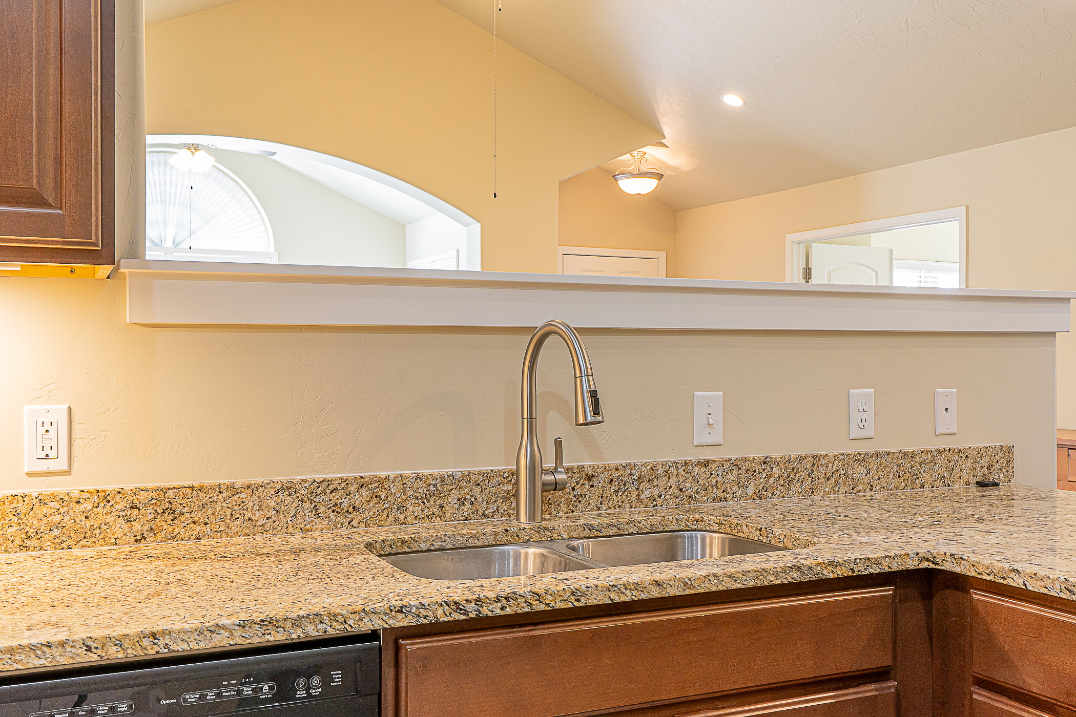 Kitchen featuring granite countertops, a double basin stainless steel sink with a high-arc faucet, and rich wood-finish cabinetry