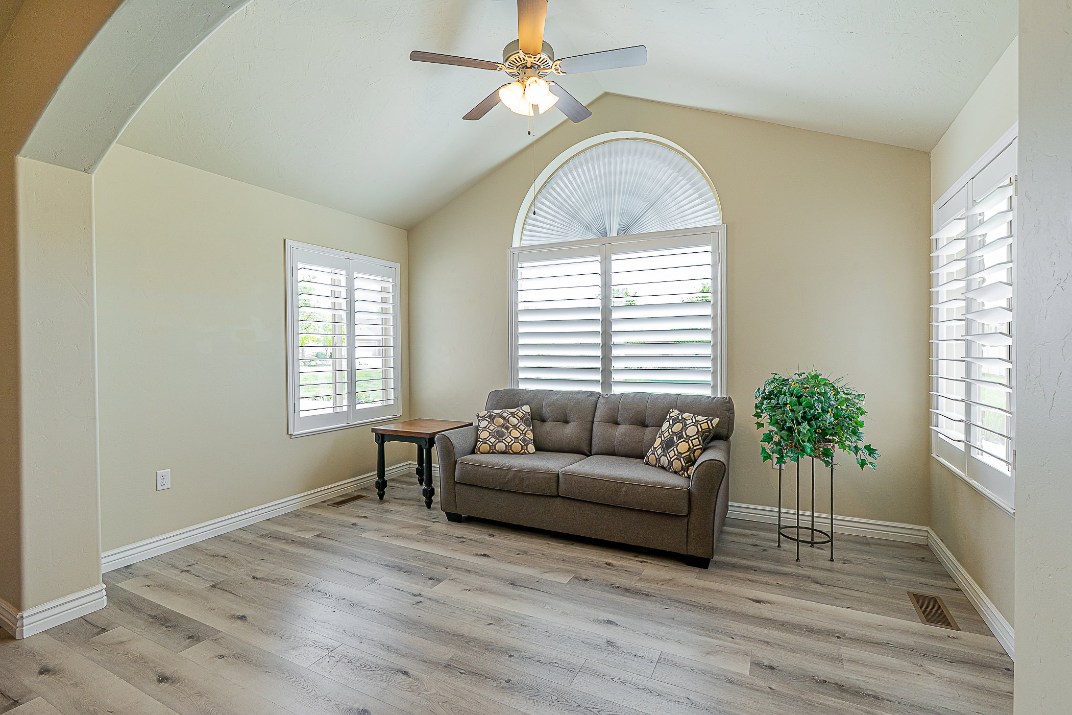 Vaulted ceiling living area featuring wood-finish flooring, an arched entry, and white plantation shutters on multiple windows, including an arched window