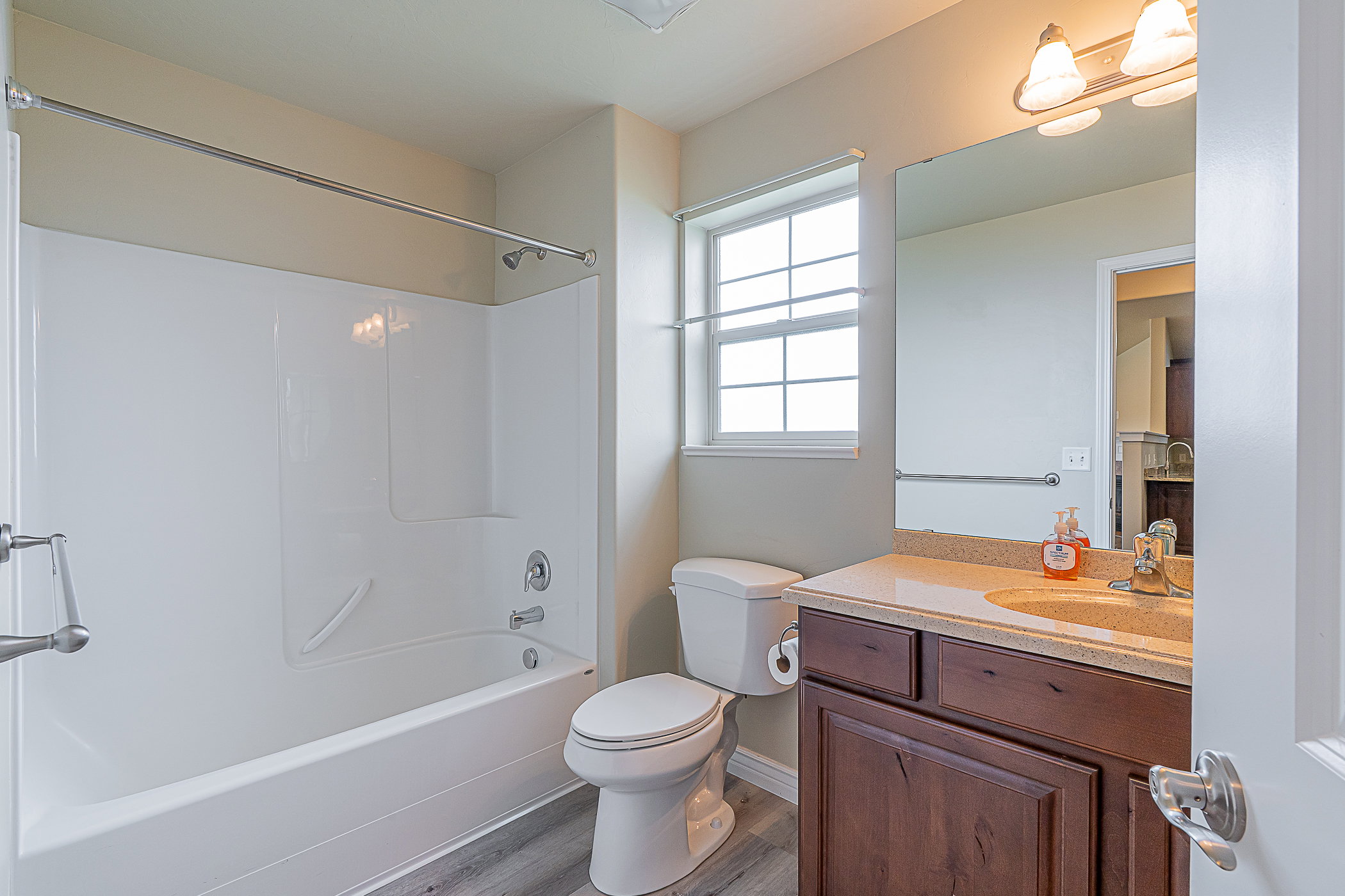 Full bathroom featuring a white tub and shower combination with chrome fixtures, a single-pane window with privacy glass, a dark wood-finish vanity with a light-colored countertop, and a large wall-mounted mirror