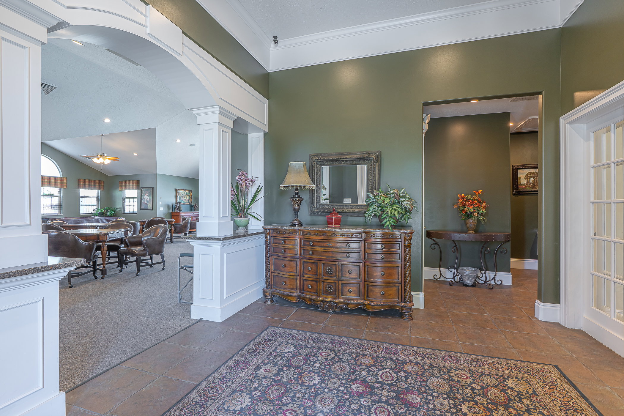 Tile flooring with a decorative area rug opens to a carpeted common area through an arched entryway with detailed millwork