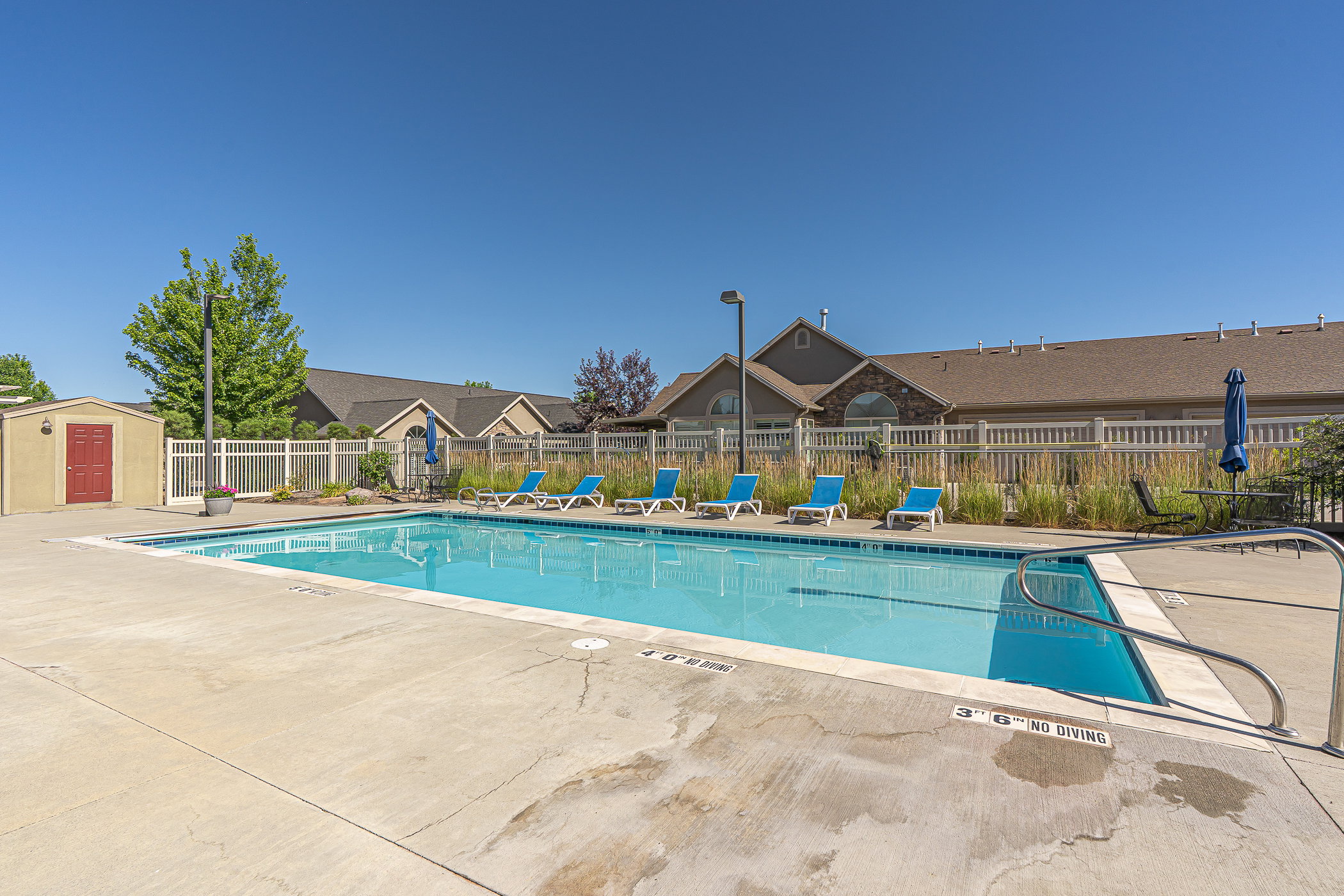 Outdoor swimming pool featuring a concrete deck, white perimeter fencing, and surrounding landscaping
