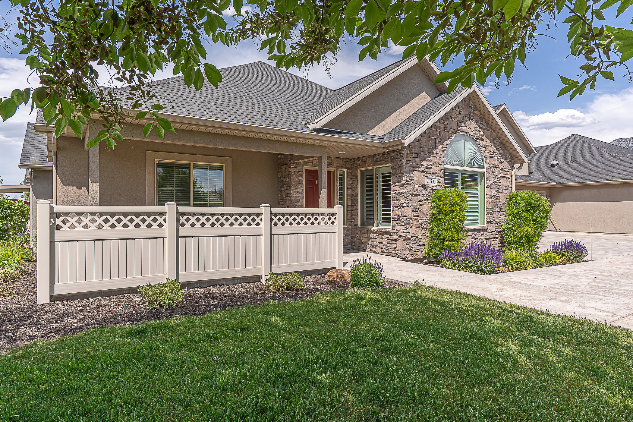 Stone facade home featuring an arched window, a covered front entry, and a lattice-top fence